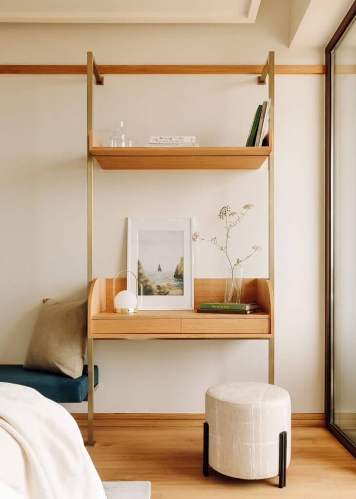 Aethos Ericeira, Portugal — Minimalist wooden shelving unit with natural light, framed landscape art, dried botanicals, and cream linen ottoman in contemporary bedroom.