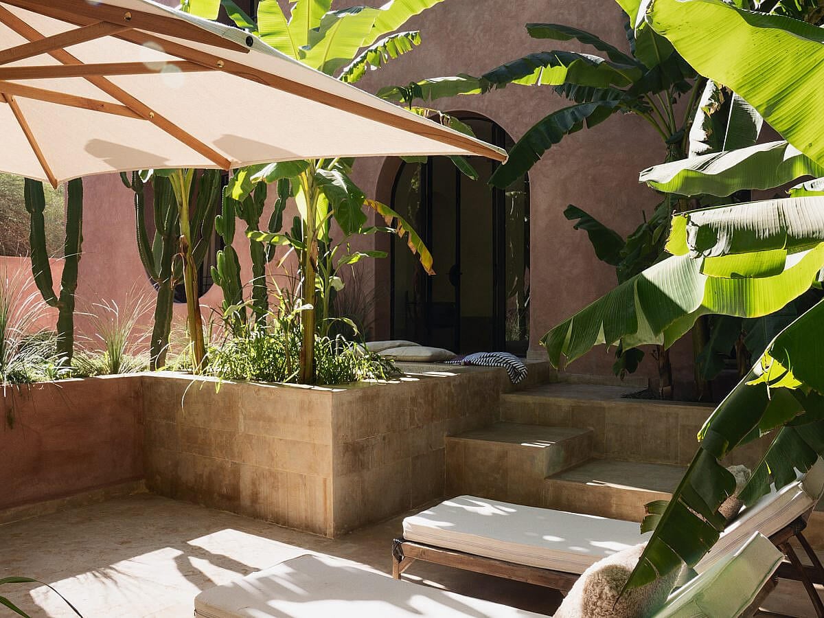 Maison Brummell Majorelle, Africa — Ochre-walled courtyard with banana plants, geometric canvas shade, concrete planters, and daybed beneath dappled sunlight.
