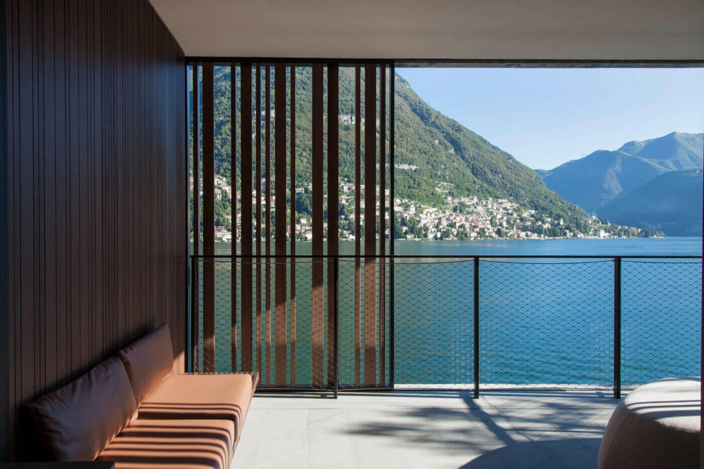 il Sereno Lago di Como, Italy — Modern lakeside terrace with wooden slat screening, minimalist furnishings, panoramic alpine lake views and forested mountainside village