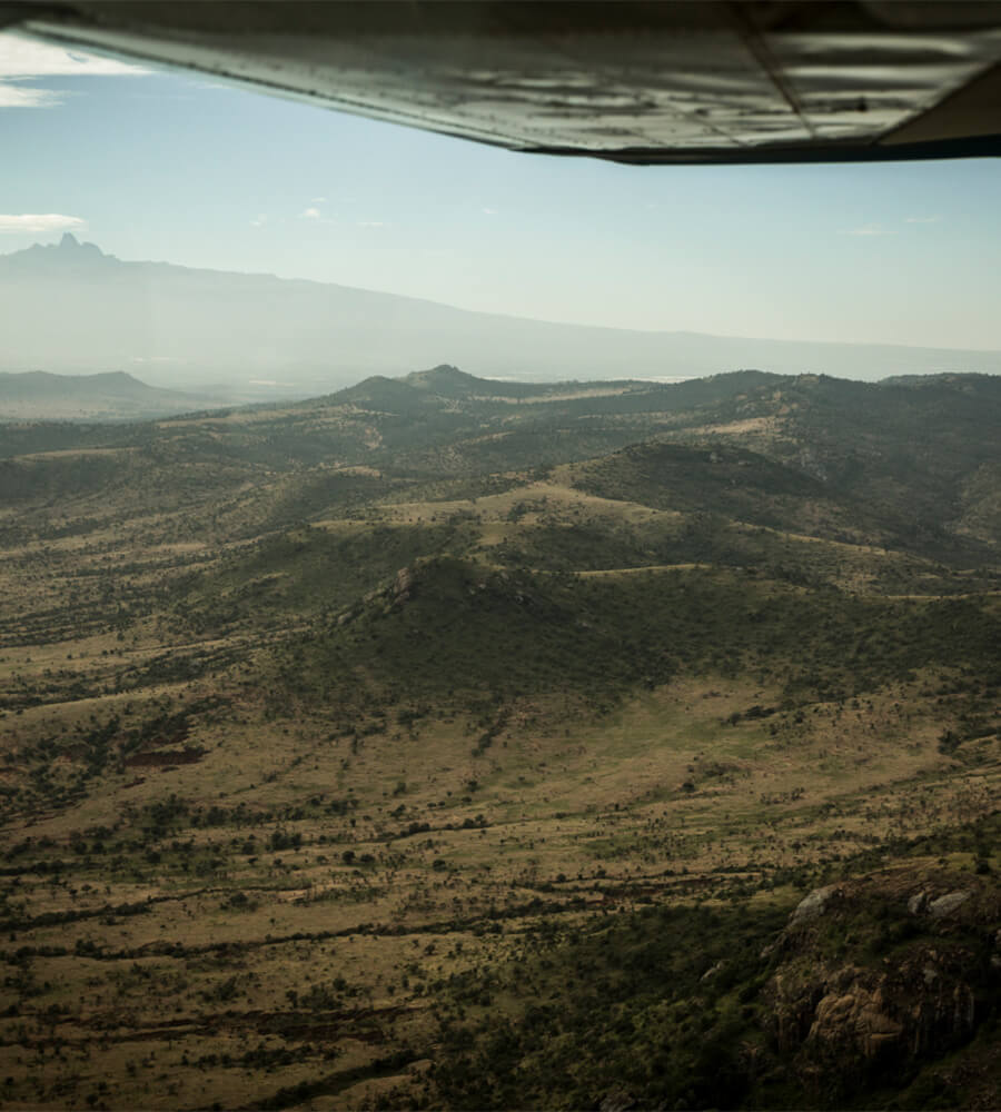 Arijiju Retreat, Africa — aerial view of rolling hills and savanna landscape with volcanic peaks and morning mist under clear sky, framed by aircraft window.