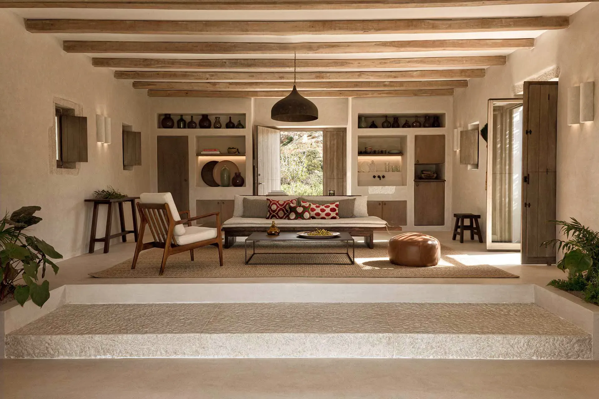 The Rooster, Europe — Minimalist villa living room with exposed wooden beams, built-in shelving, mid-century furniture, and natural light from garden doors.