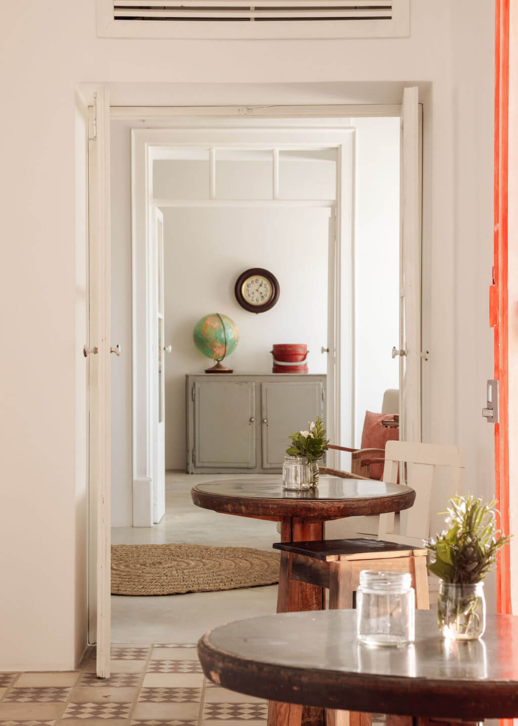 Hospedaria, Europe — Enfilade of white-trimmed doors framing vintage globe, wall clock, and gray cabinetry, with round wood tables and natural light creating layered spatial depth.