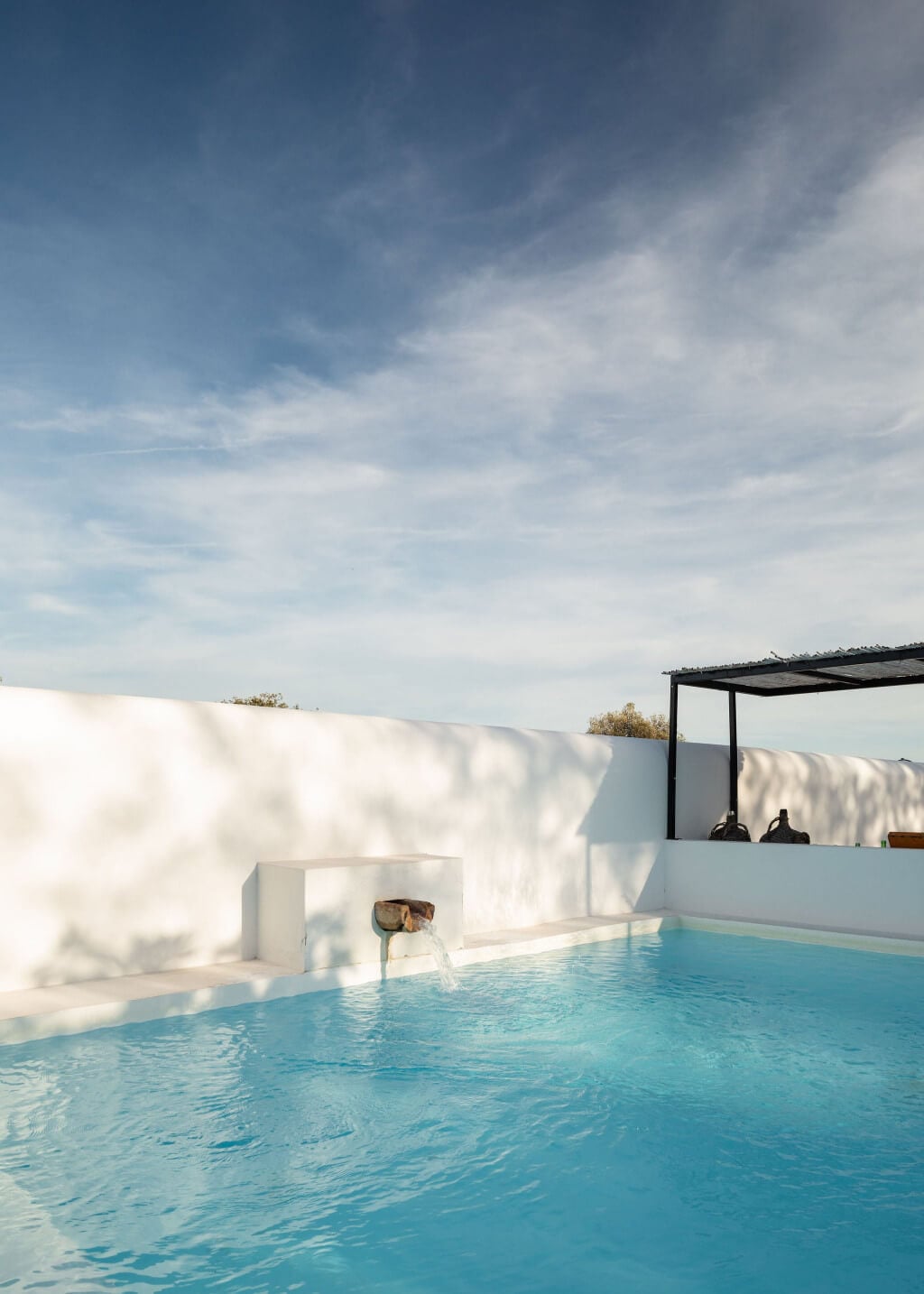 Hospedaria, Europe — Minimalist white courtyard with turquoise swimming pool, architectural shadow play, and contemporary pergola under clear sky.