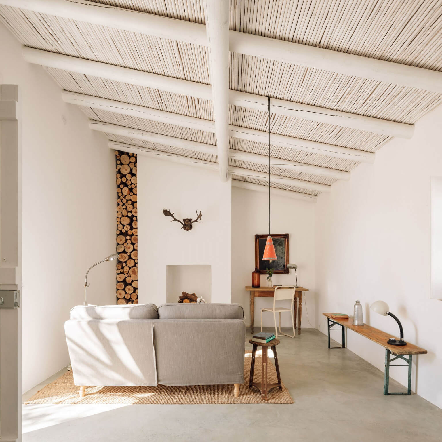 Hospedaria, Europe — Minimalist living space with exposed beam ceiling, natural light, linen sofa, wooden storage wall, and curated vintage furnishings.