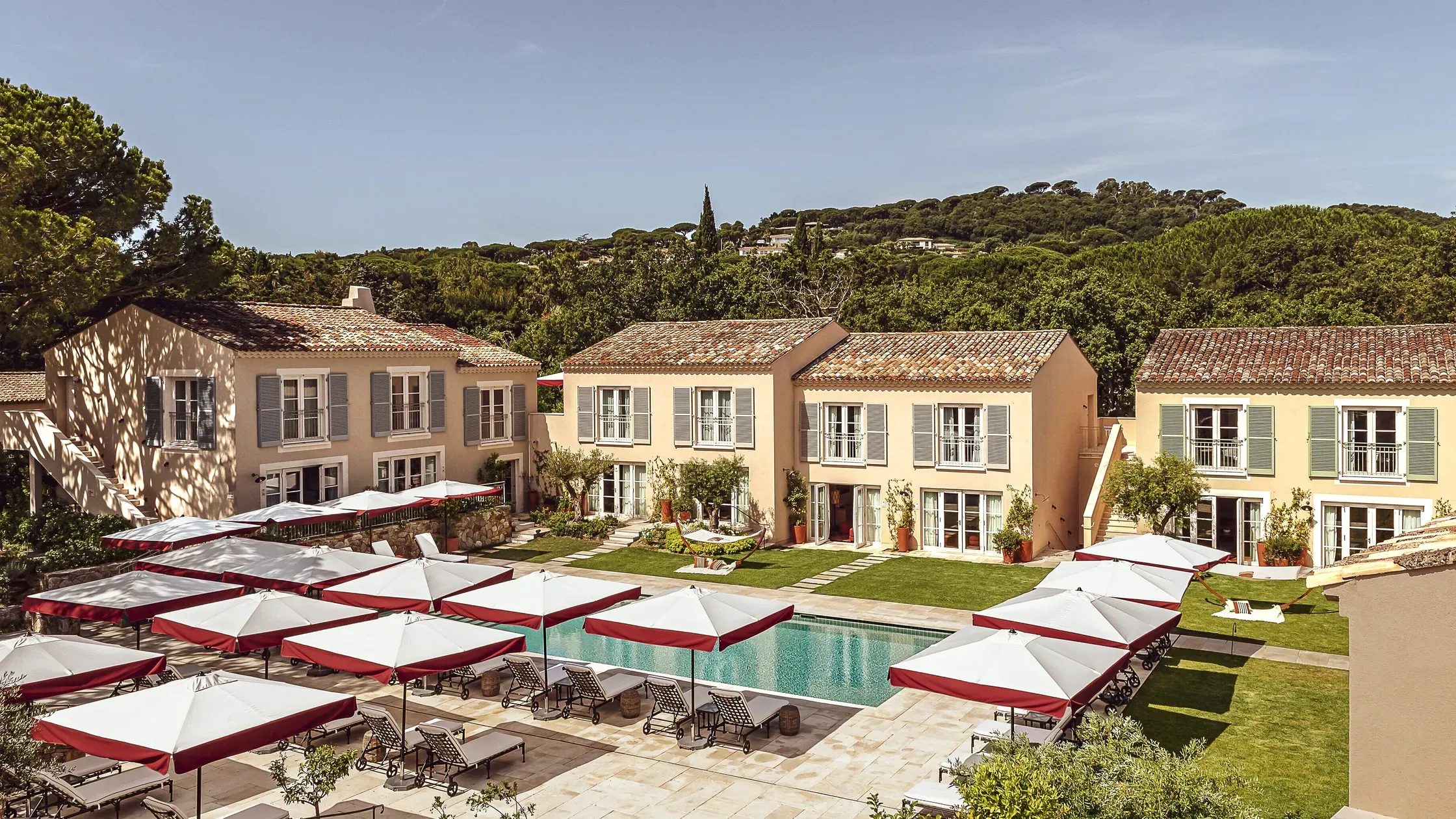 Hôtel Lou Pinet, Europe — Ochre villas with terracotta roofs overlook a swimming pool framed by burgundy-and-white umbrellas on a sun-drenched Mediterranean terrace.