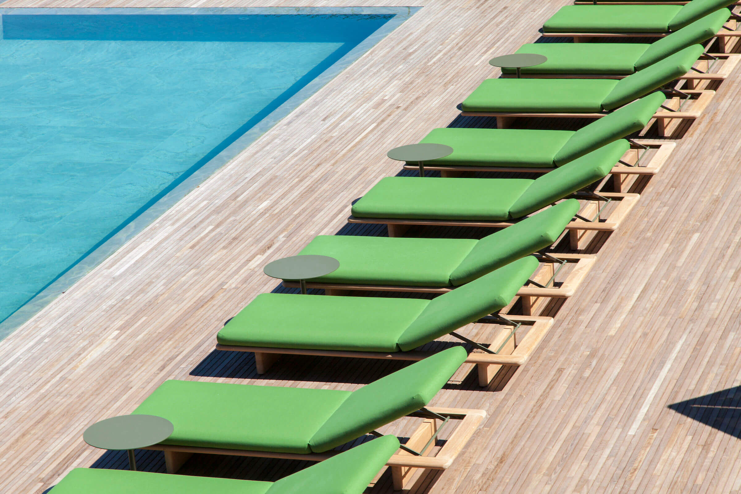 il Sereno Lago di Como, Lake Como, Italy — Lime green sunloungers with side tables lined along wooden deck beside turquoise pool.