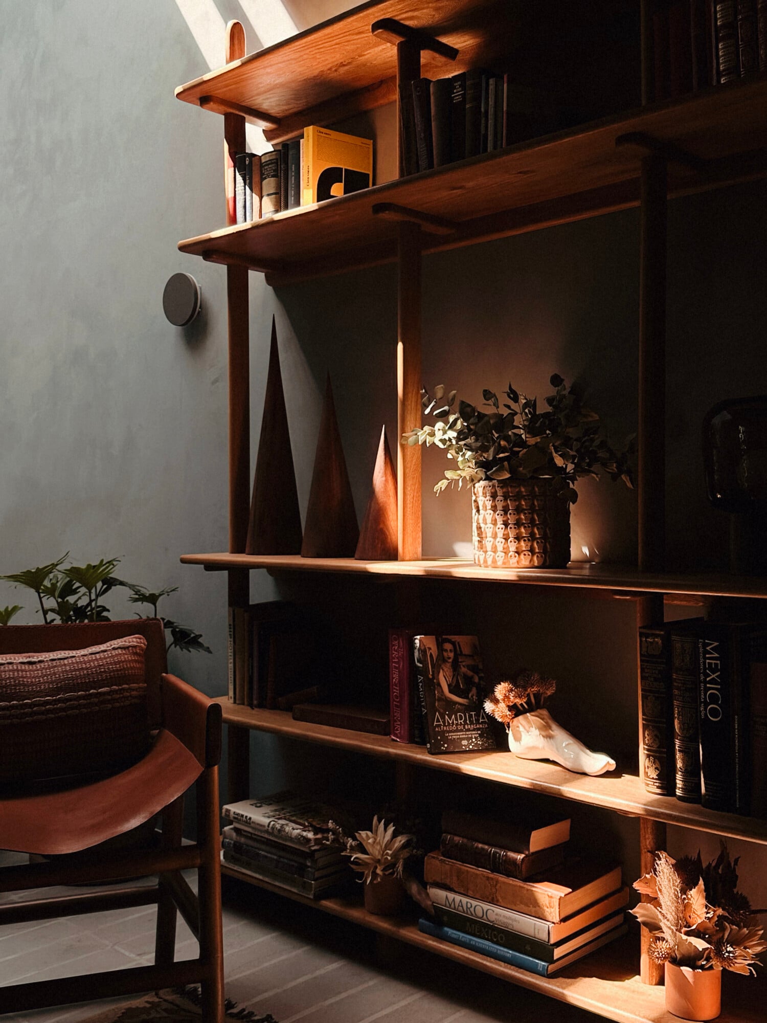 UMA Casa, Mexico — Wooden shelving unit with stacked books, woven basket planter, and ceramic vessels illuminated by natural light, mid-century modern design.
