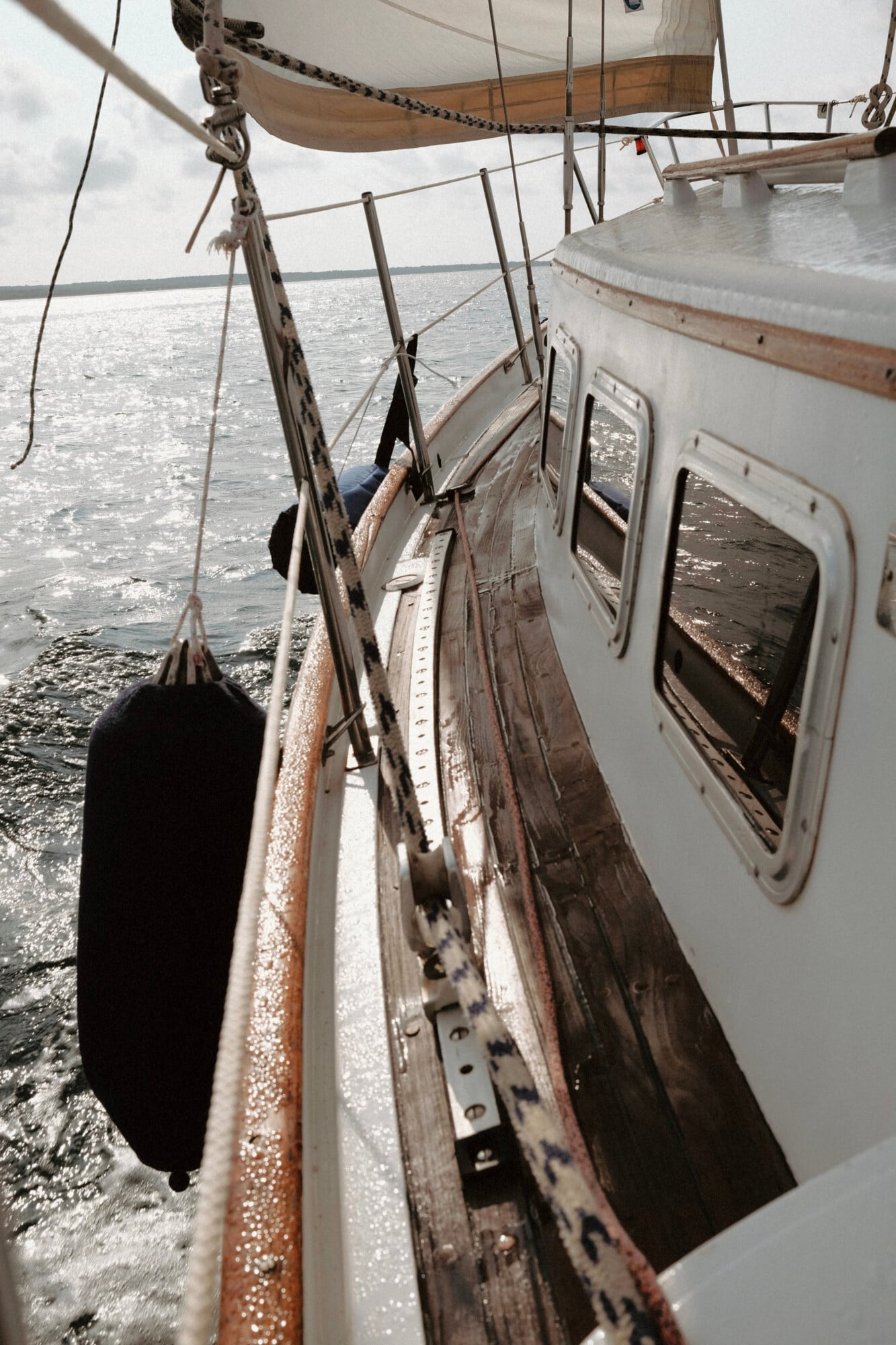 Rapita Charter, Balearic Islands — Sailboat deck with weathered wooden rail, rope rigging, and calm Mediterranean waters under overcast sky.