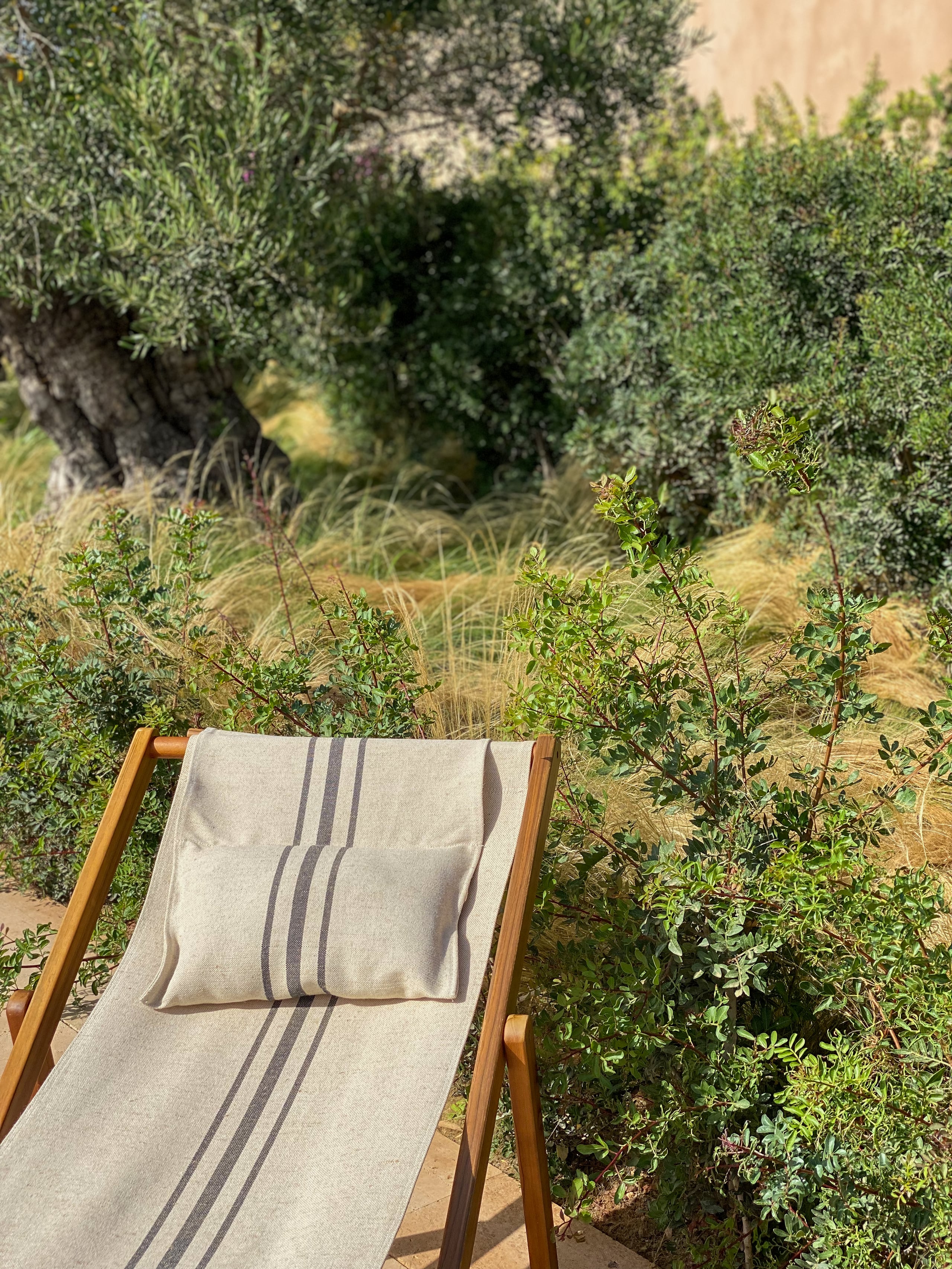 Can Ferrereta, Balearic Islands — Wooden deckchair with striped linen upholstery positioned among Mediterranean herbs and olive trees in sunlit garden.