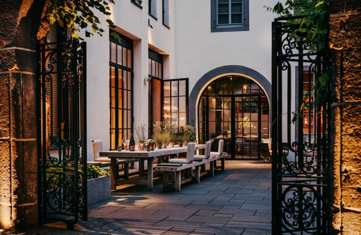 Purs Restaurant, Europe — Candlelit courtyard dining with arched stone doorway, black iron gates, limestone walls, and wooden table seating at dusk.