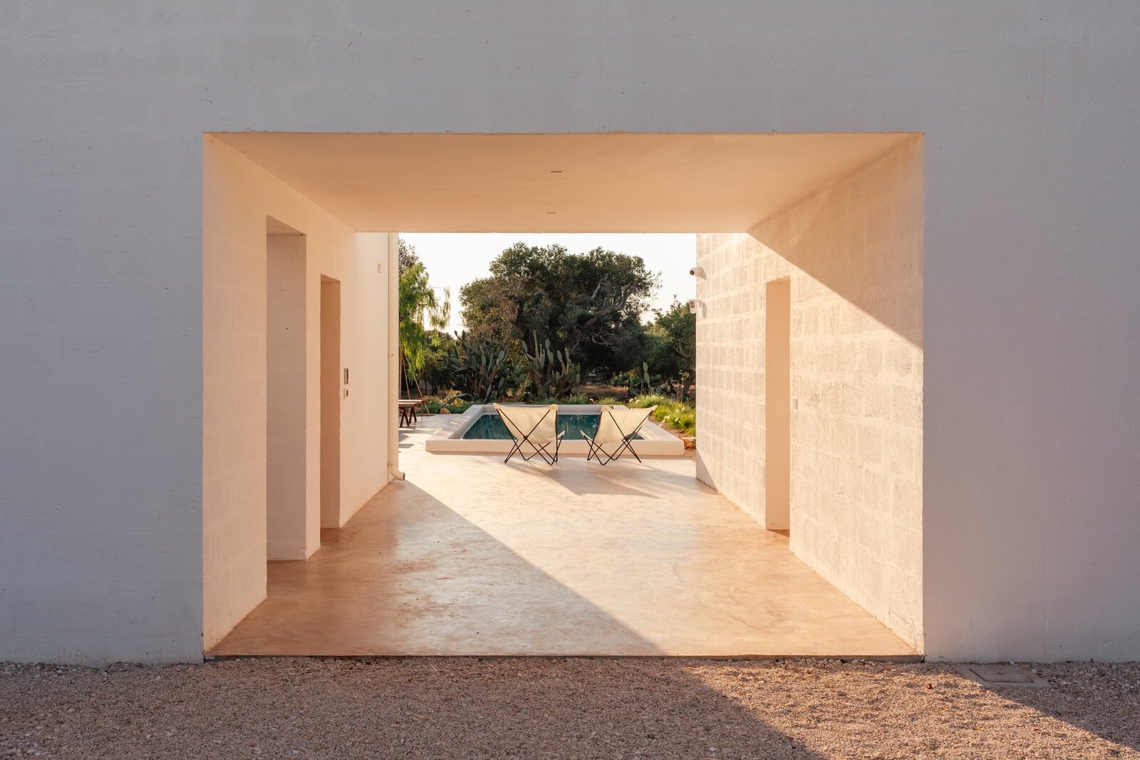 Casanguilla, Europe — Minimalist terracotta corridor framing pool and gardens, natural light casting geometric shadows on warm stone flooring.