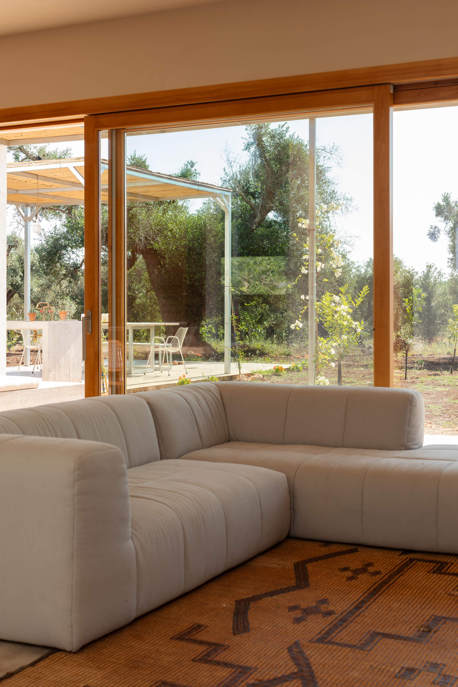 Casanguilla, Europe — Curved cream sectional sofa with ribbed upholstery facing floor-to-ceiling glazed doors opening onto terracotta pergola and olive grove landscape.