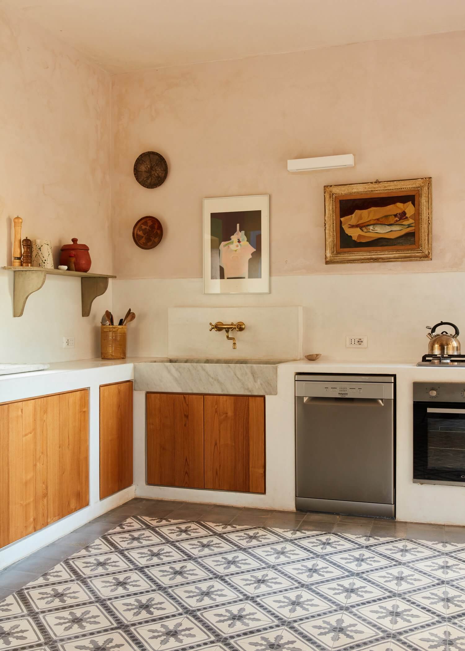 Parco Dei Sesi, Europe — Minimalist kitchen with wooden cabinetry, marble sink, patterned cement floor, and curated wall art in warm neutral tones.