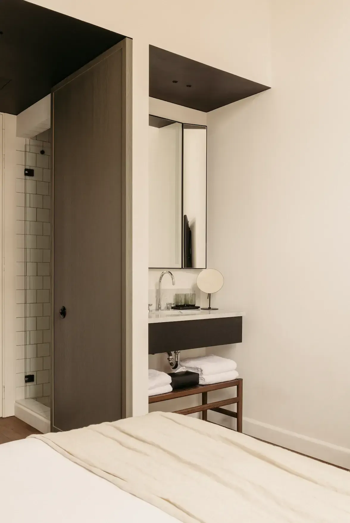 August, Europe — Modern luxury bathroom with dark ceiling plane, floating black vanity, rectangular mirror, marble countertop, and minimalist wood-frame towel shelf.