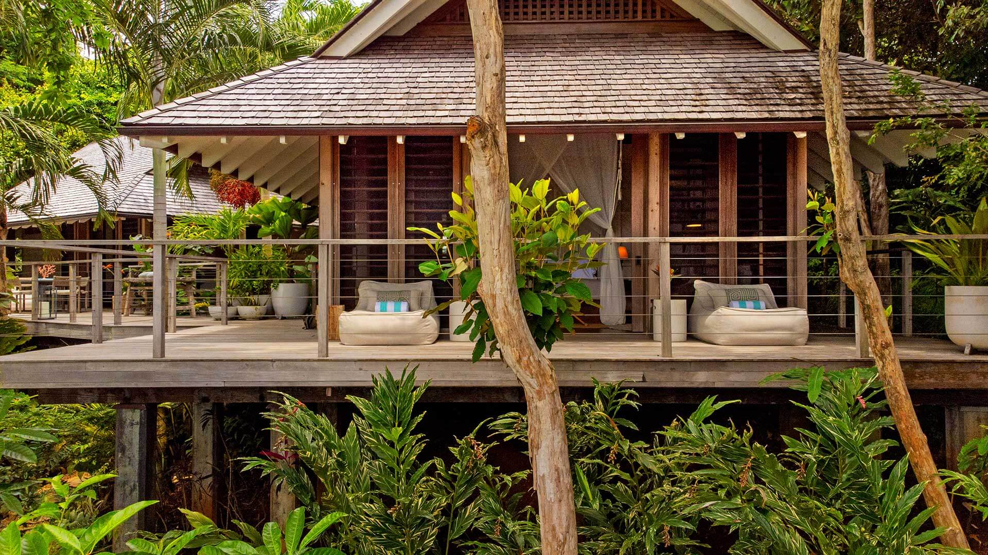 Islas Secas — Elevated wooden pavilion with louvered doors, teak posts, and woven loungers on a covered deck overlooking tropical vegetation.