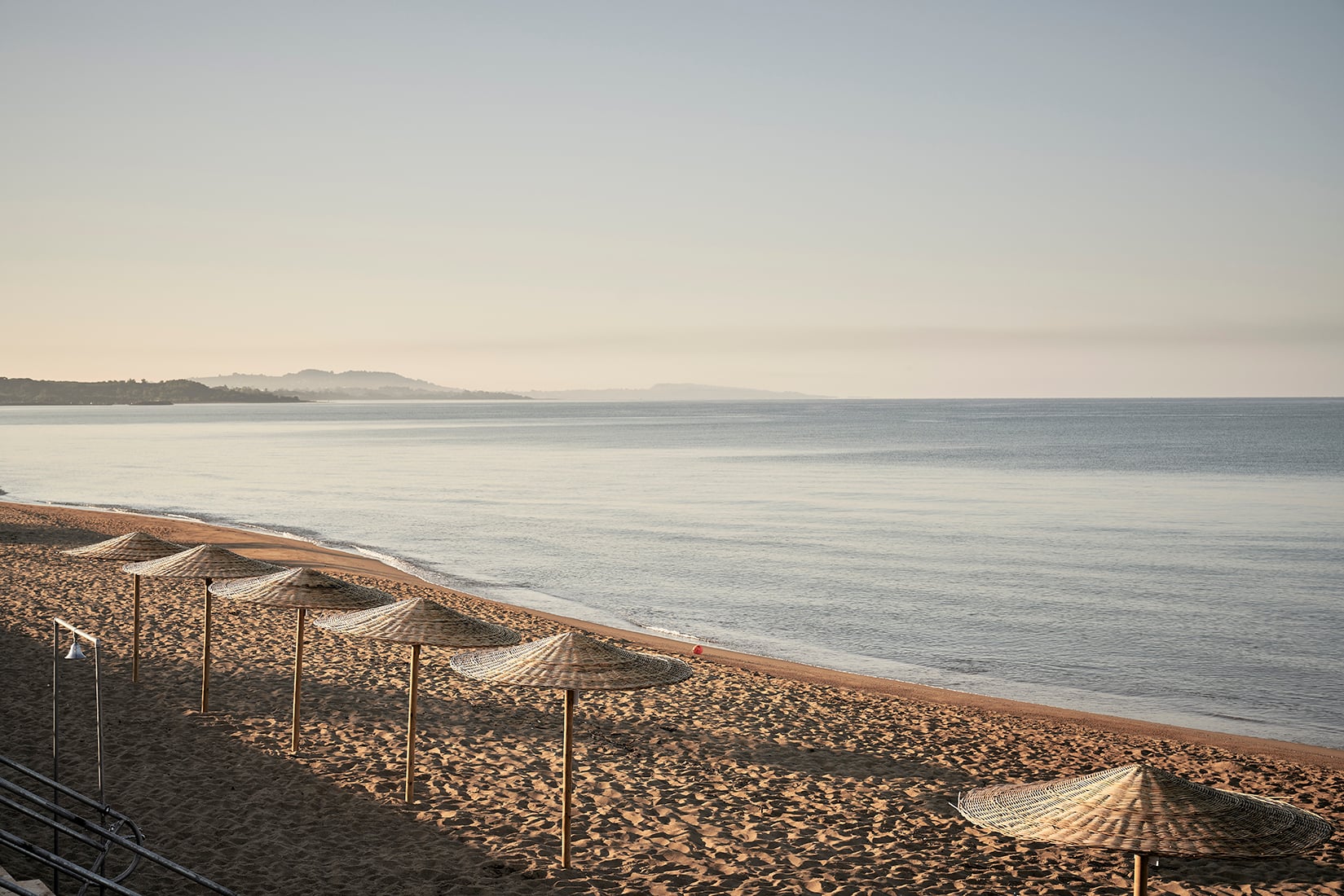 The Beach — Beach umbrellas and loungers on sandy shore at sunset with calm sea and distant coastline, The Beach, Europe — luxury coastal hospitality design.
