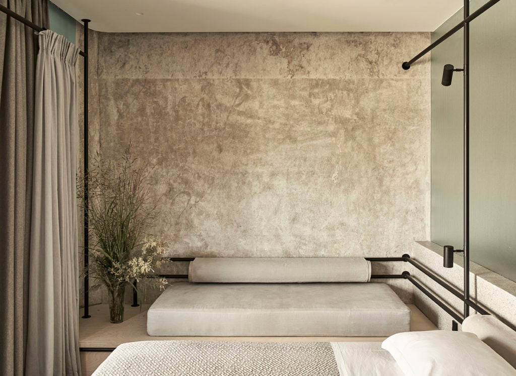 Dexamenes Seaside Hotel, Europe — Minimalist bedroom with textured concrete wall, platform bed, black metal railings, and floor-to-ceiling shower enclosure.