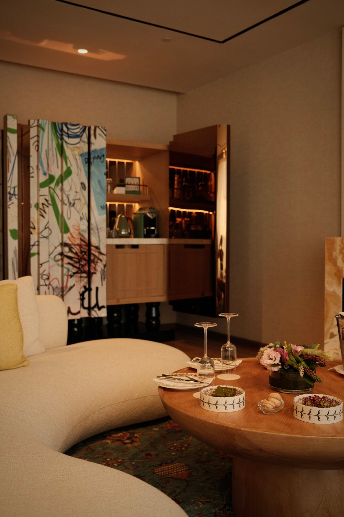 Aliée Istanbul, Turkey — Curved cream seating with wooden table, decorative bowls, fresh flowers, and illuminated shelving in warm-lit contemporary hospitality interior.