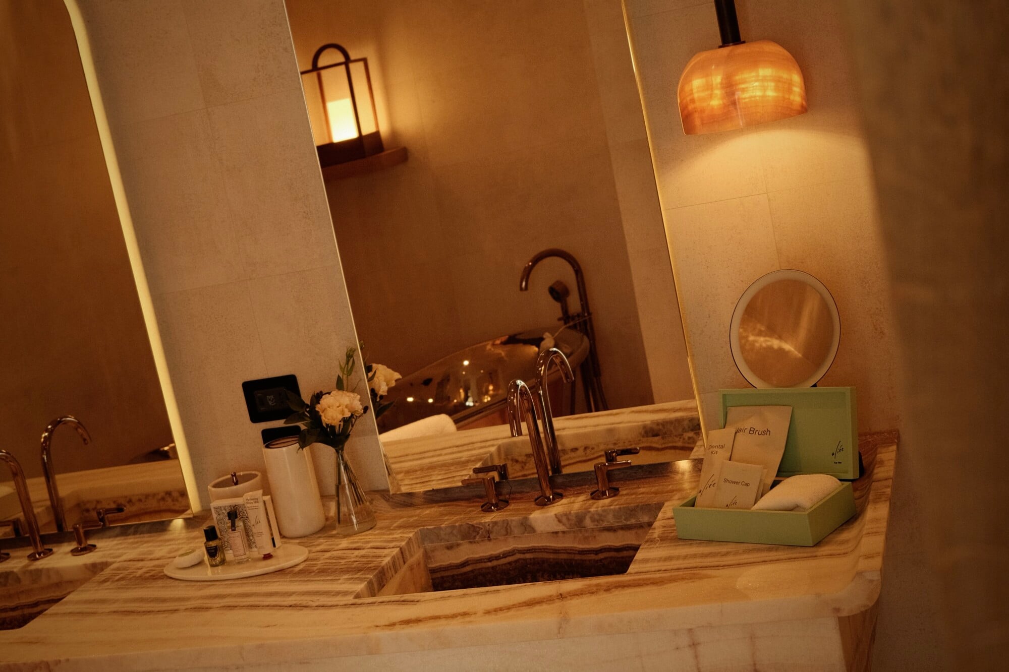 Aliée Istanbul, Turkey — Marble bathroom vanity with vessel sink, bronze fixtures, pendant lighting, mirror, white flowers, and amenity displays in warm ambient light.