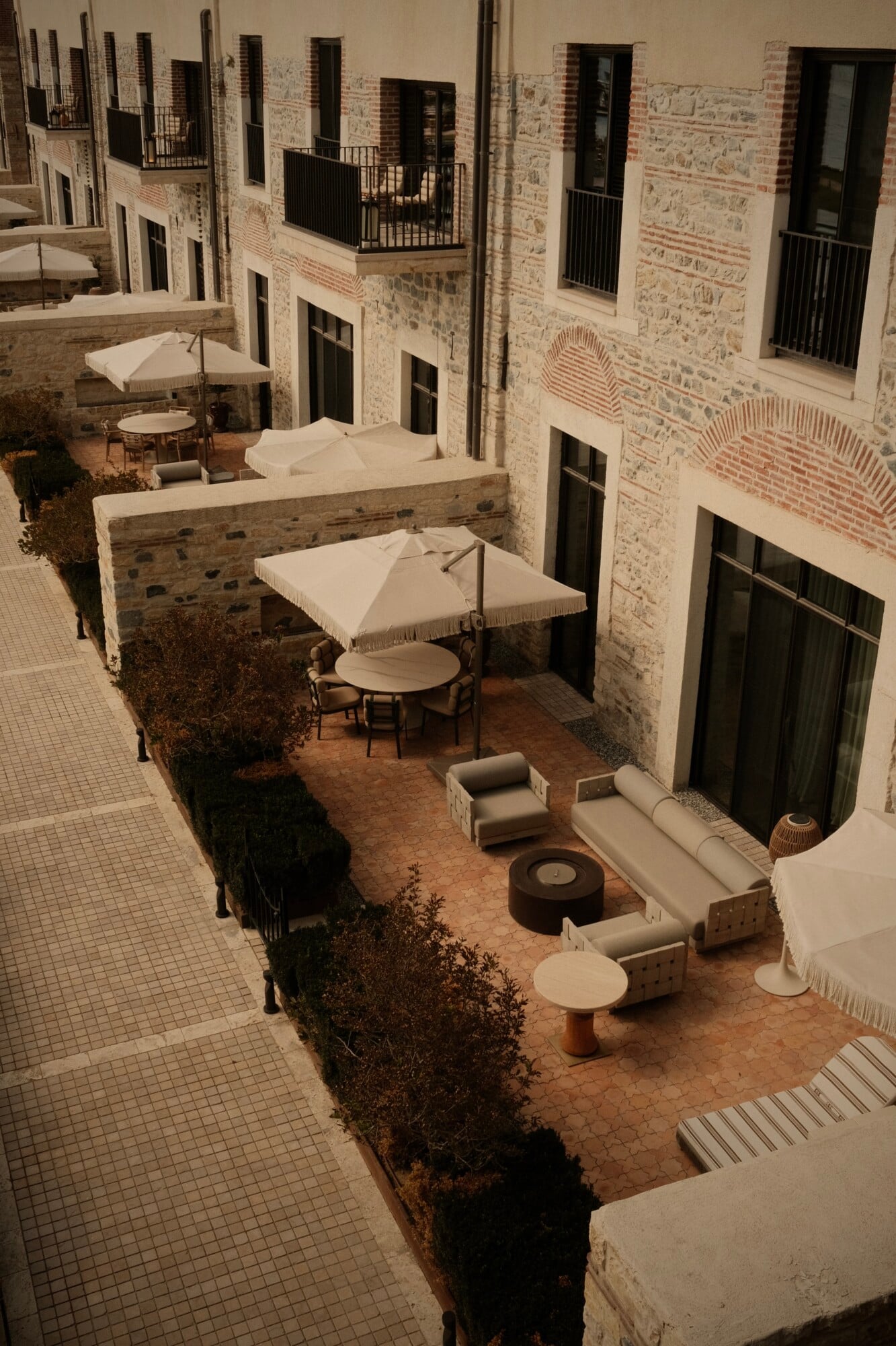 Courtyard at Aliée Istanbul with stone façades, umbrellas, linen seating, and terracotta paving framed by hedges.