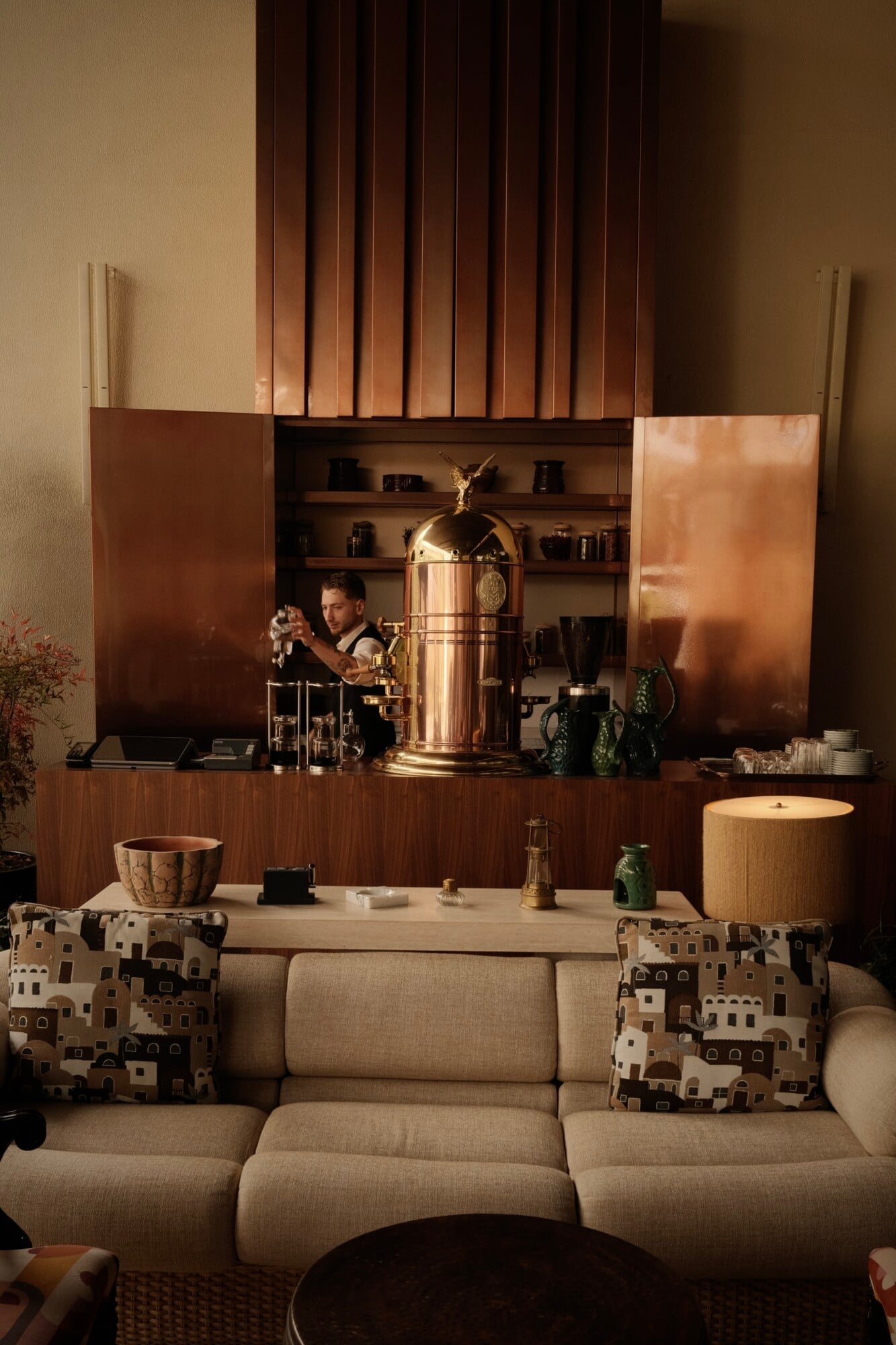 Aliée Istanbul, Istanbul, Turkey — Luxe living room with curved beige sofa, brass coffee service, wood-paneled bar counter, architectural shelving, warm ambient lighting