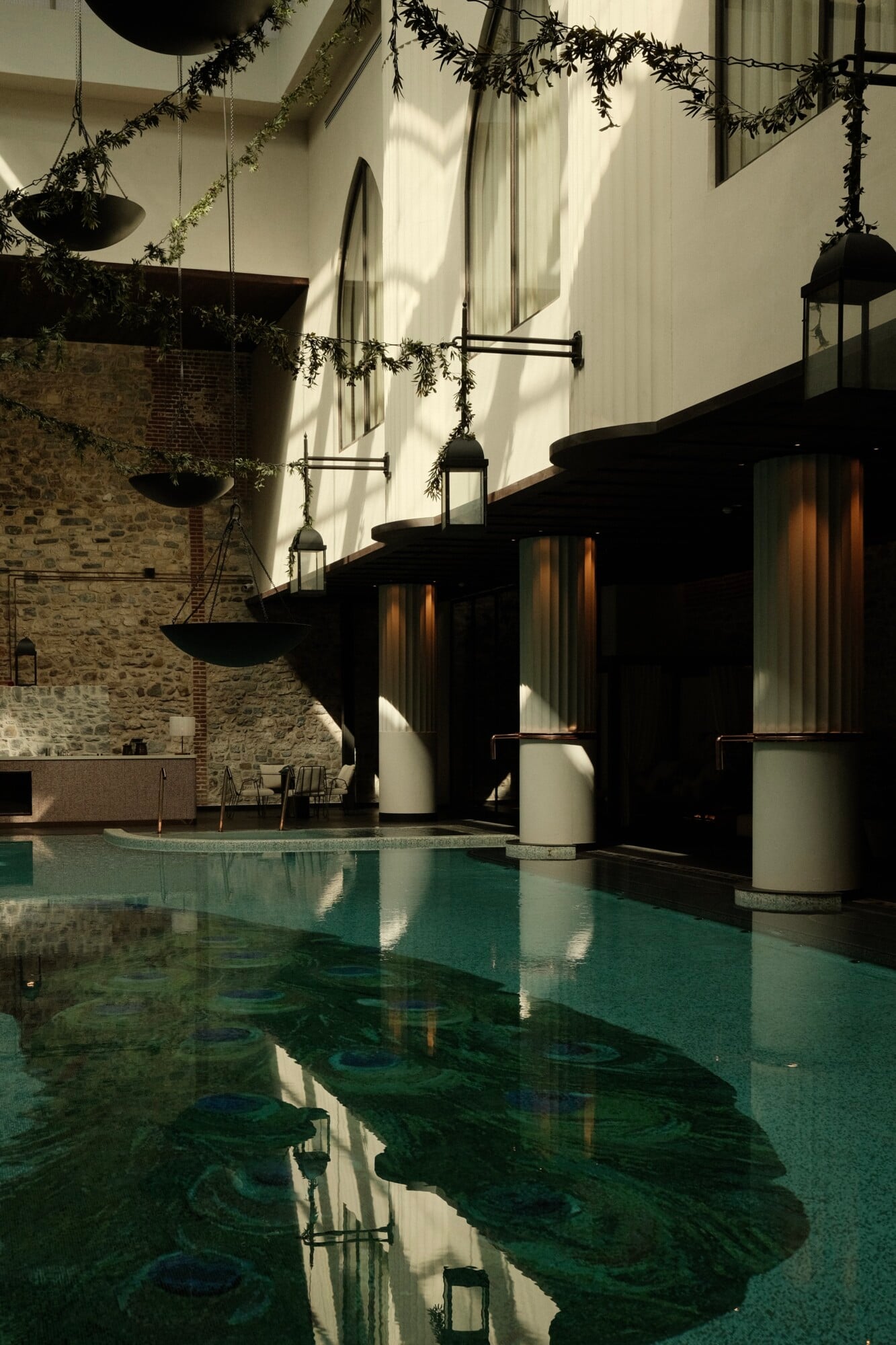 Well+ Clinic, Asia — Minimalist indoor pool with teal water, brick and white walls, hanging greenery, black wooden structures, natural light, luxury wellness architecture.