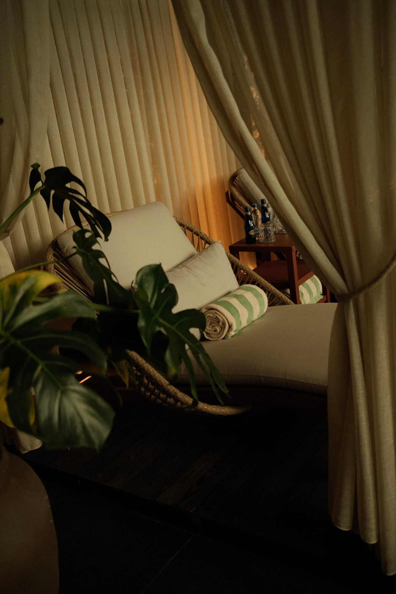 Aliée Istanbul, Turkey — Canopied daybed with cream pillows and striped cushions, potted plant, wooden side table, warm window light through sheer curtains.