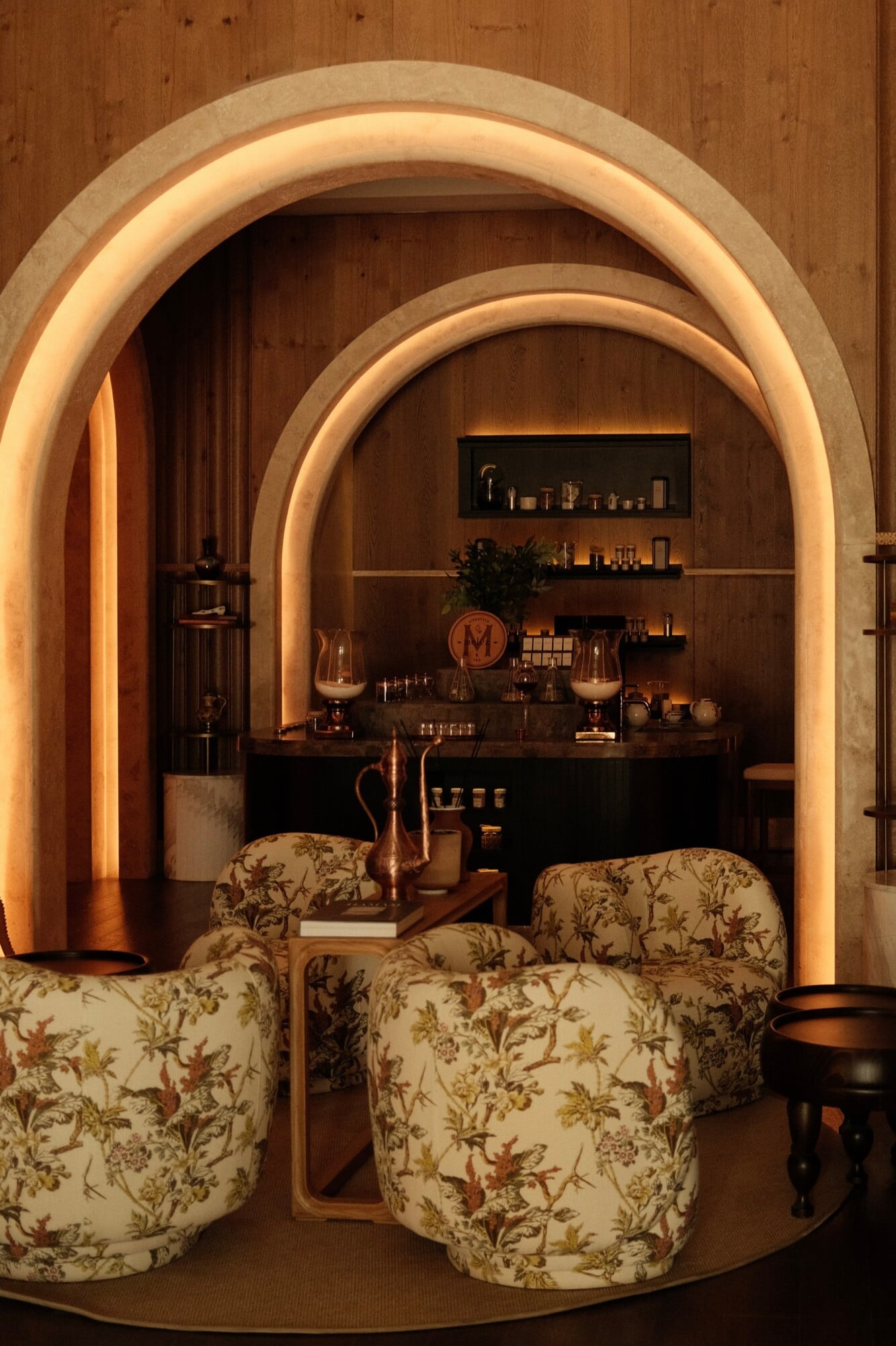 Well+ Lounge, Asia — Arched stone alcove with warm ambient lighting, floral upholstered seating, dark bar counter, and tiered shelving in luxury wellness lounge.
