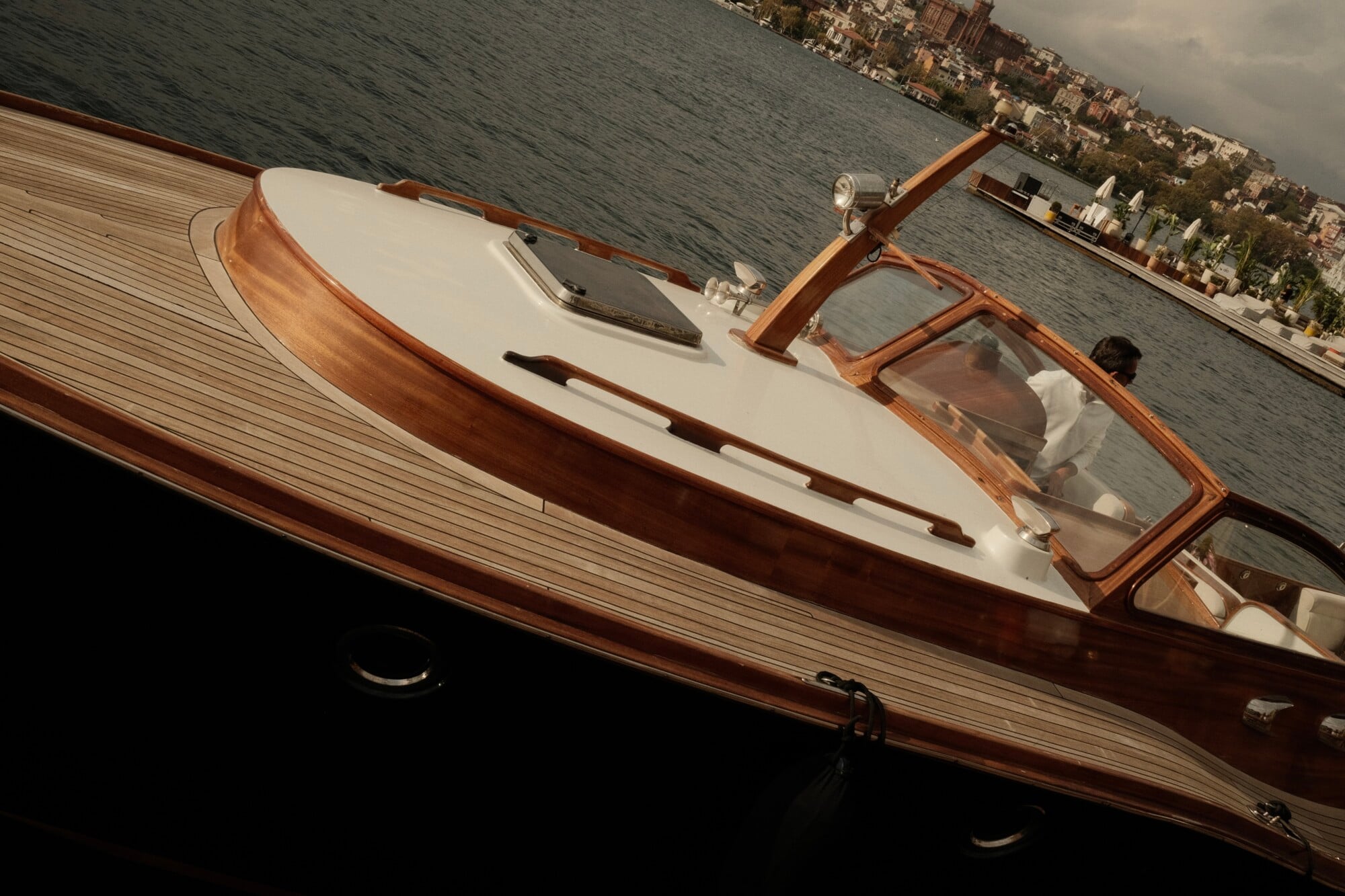Sail the Bosphorus — Vintage wooden yacht with cream hull moored on the Bosphorus, Istanbul, with waterfront cityscape and natural light.