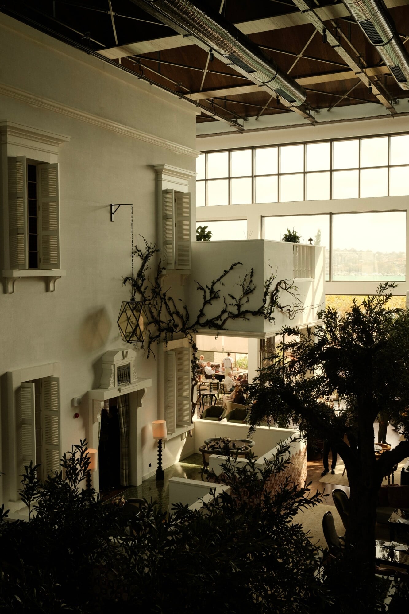Aliée Istanbul, Istanbul, Turkey — Minimalist atrium with soaring windows, sculptural dried botanicals, concrete terraces, and industrial ceiling details flooded with natural light.