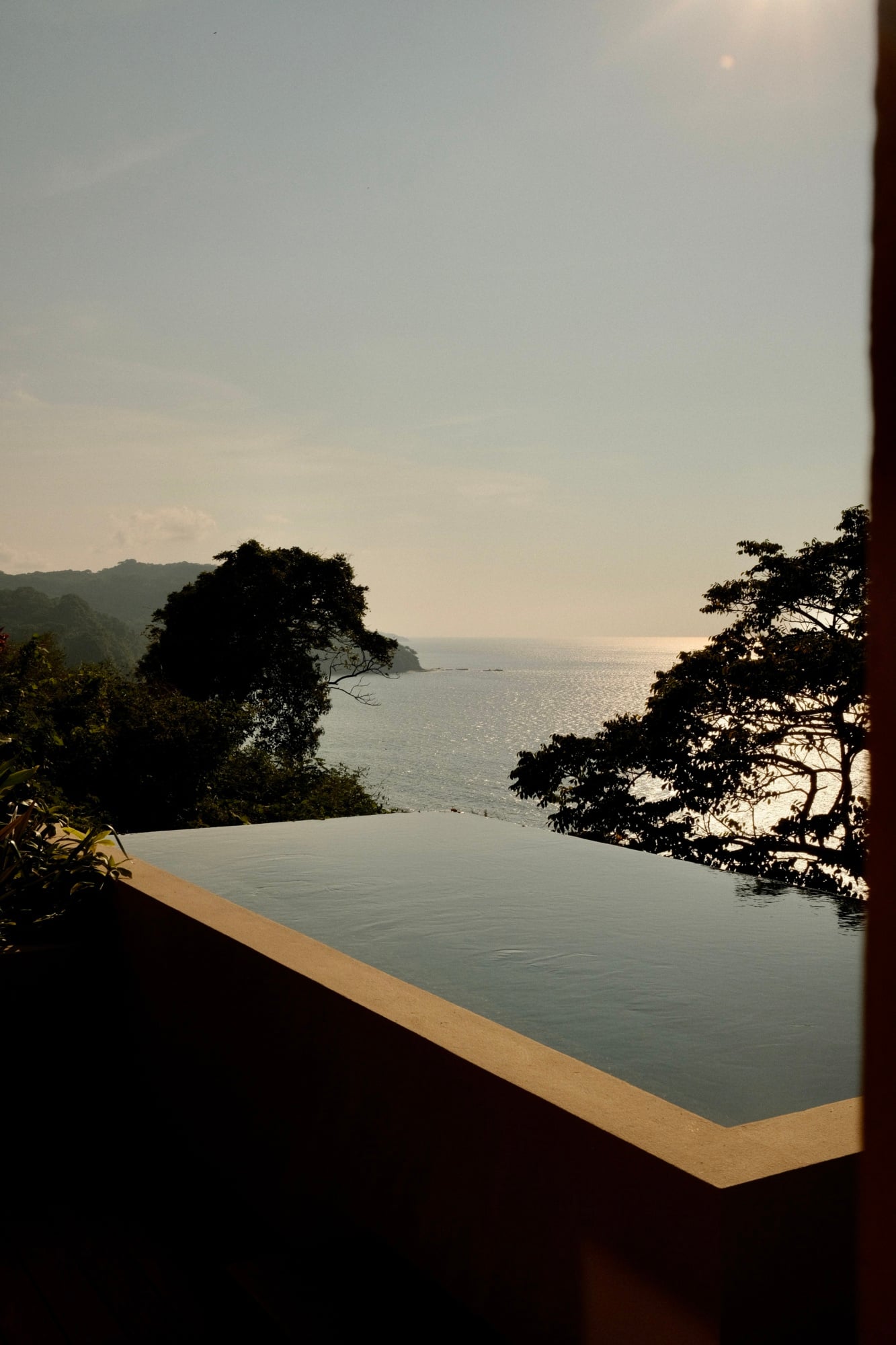Rosewood Mandarina, Mexico — infinity pool overlooking tropical coastline and forested cliffs at sunset, minimalist concrete edge framing ocean vista