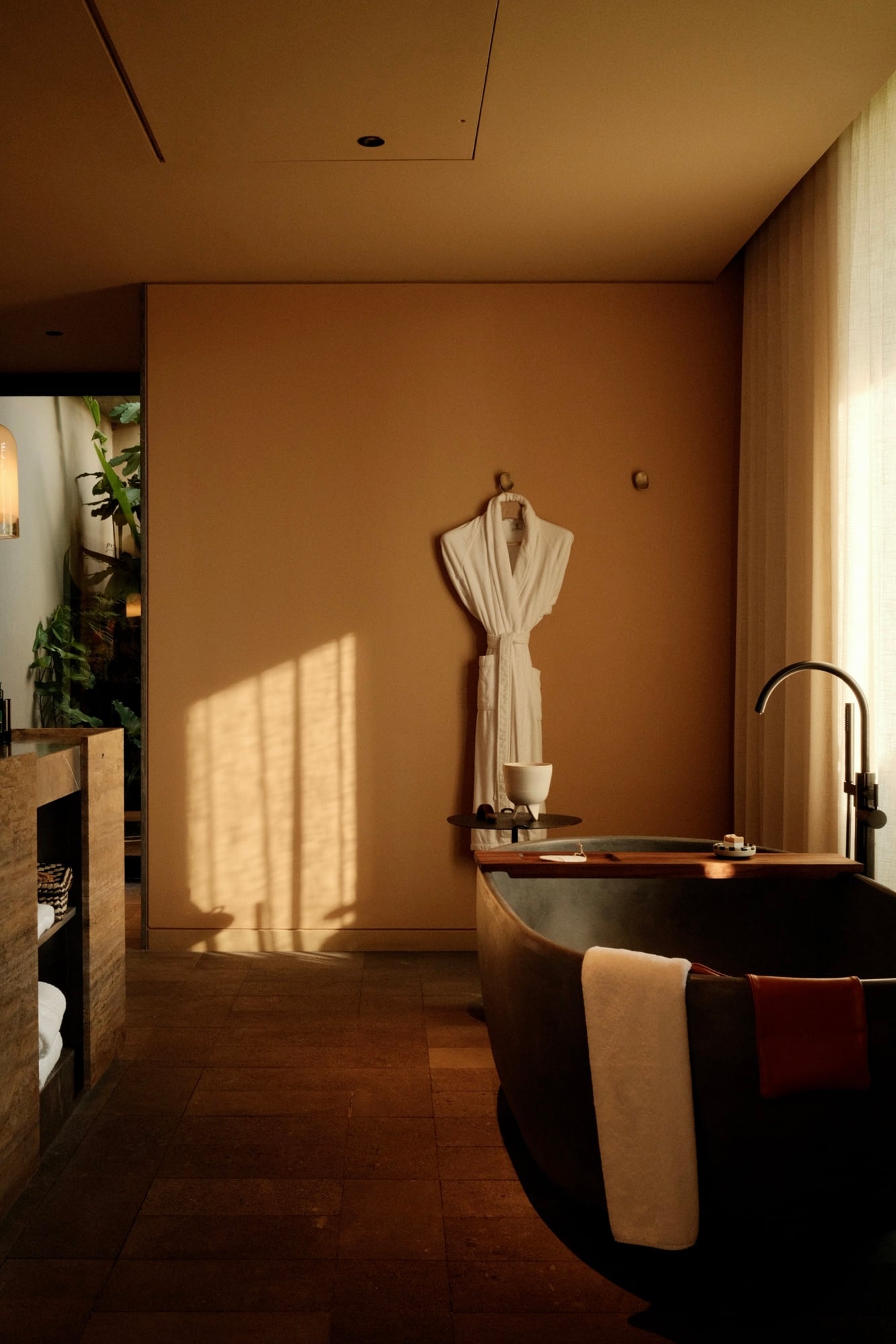 Rosewood Mandarina, Mexico — Spa bathroom with terracotta walls, freestanding black soaking tub, natural light, minimalist luxury design, warm earthy aesthetic.