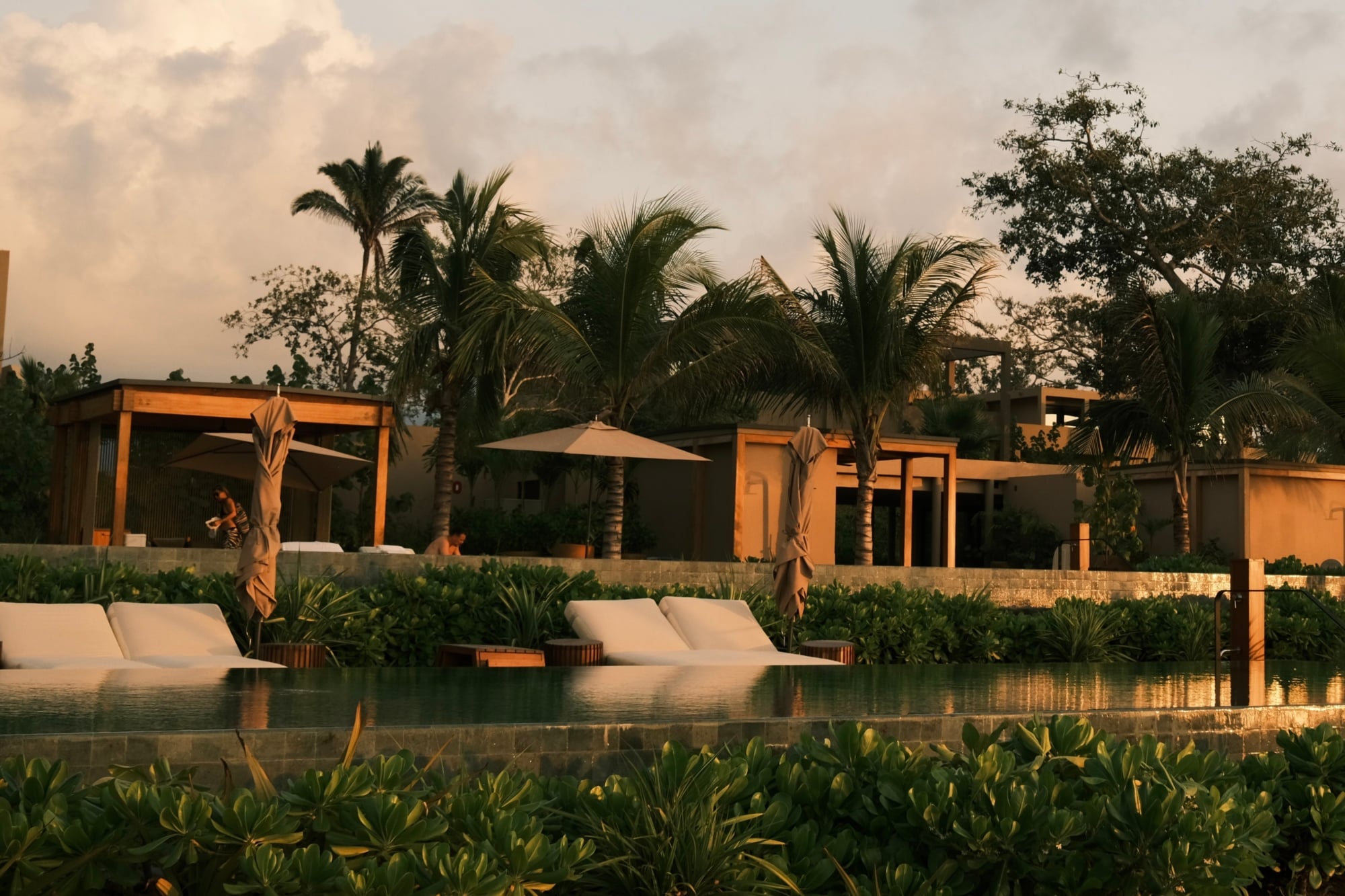Rosewood Mandarina, Mexico — Modernist ochre pavilions with infinity pool, palm trees, and layered landscaping at golden hour.