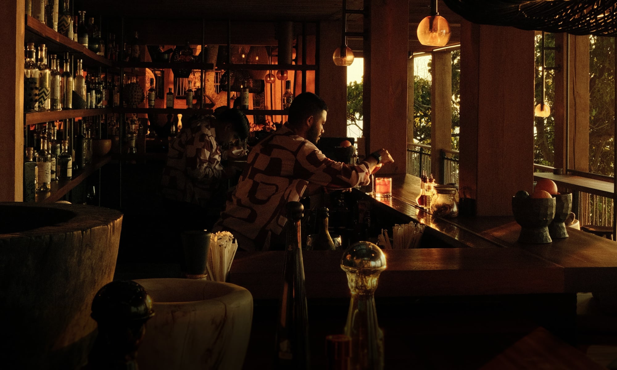 Rosewood Mandarina, Mexico — Candlelit bar interior with pendant lighting, wooden counter, open-air terrace views, warm ambient glow at dusk.