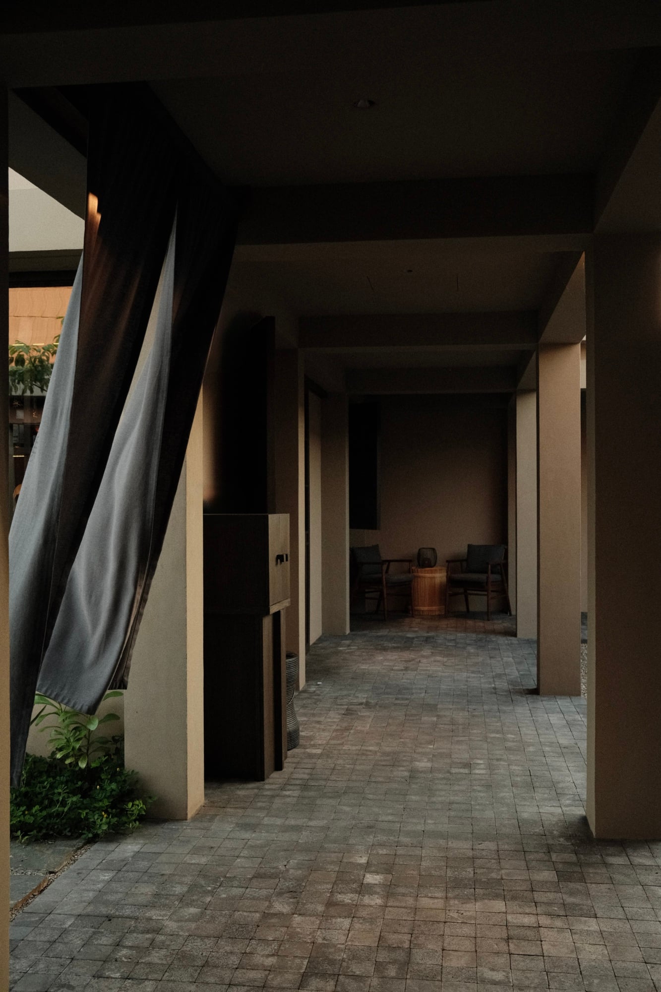 Rosewood Mandarina, Mexico — Minimalist covered walkway with cream walls, geometric shadows, brick flooring, and dark ceiling creating serene architectural passage.