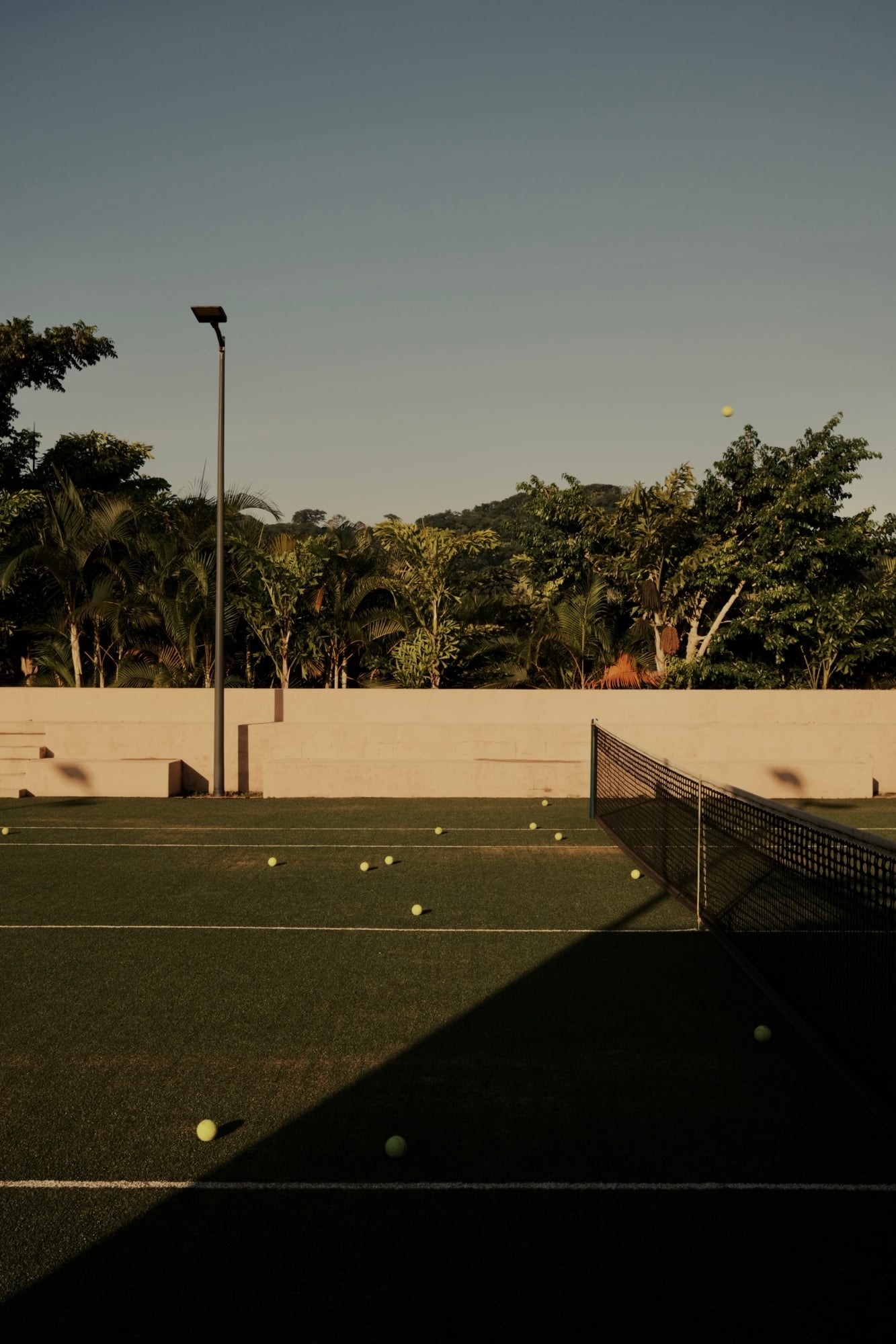 Tennis & Paddle Club, Mexico — Empty clay courts with scattered tennis balls, modern concrete pavilion, and lush tropical vegetation under golden afternoon light.