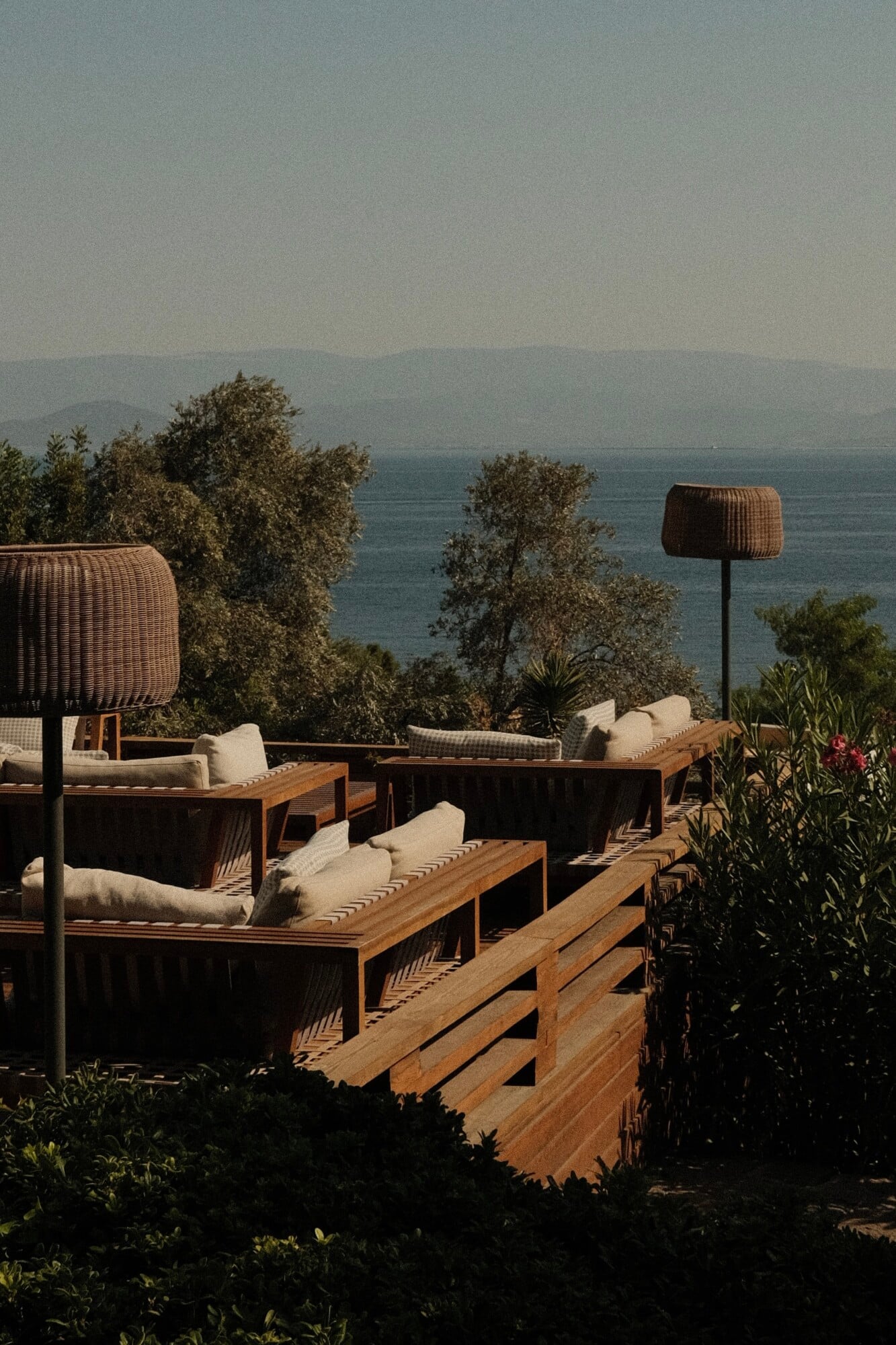 Mandarin Oriental Bodrum, Turkey — Wooden lounge seating with cream cushions and woven pendant lights overlooking the Aegean Sea, afternoon light filtering through olive trees.