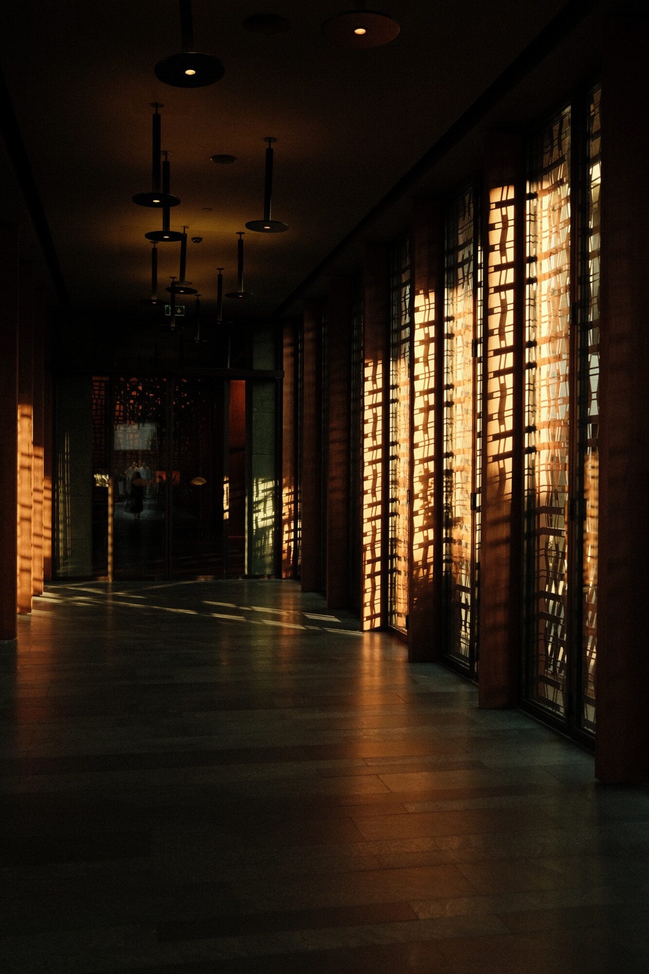 Mandarin Oriental Bodrum, Asia — Illuminated lattice screens cast geometric shadows across dark corridor, pendant lights suspended from coffered ceiling, warm ambient glow.