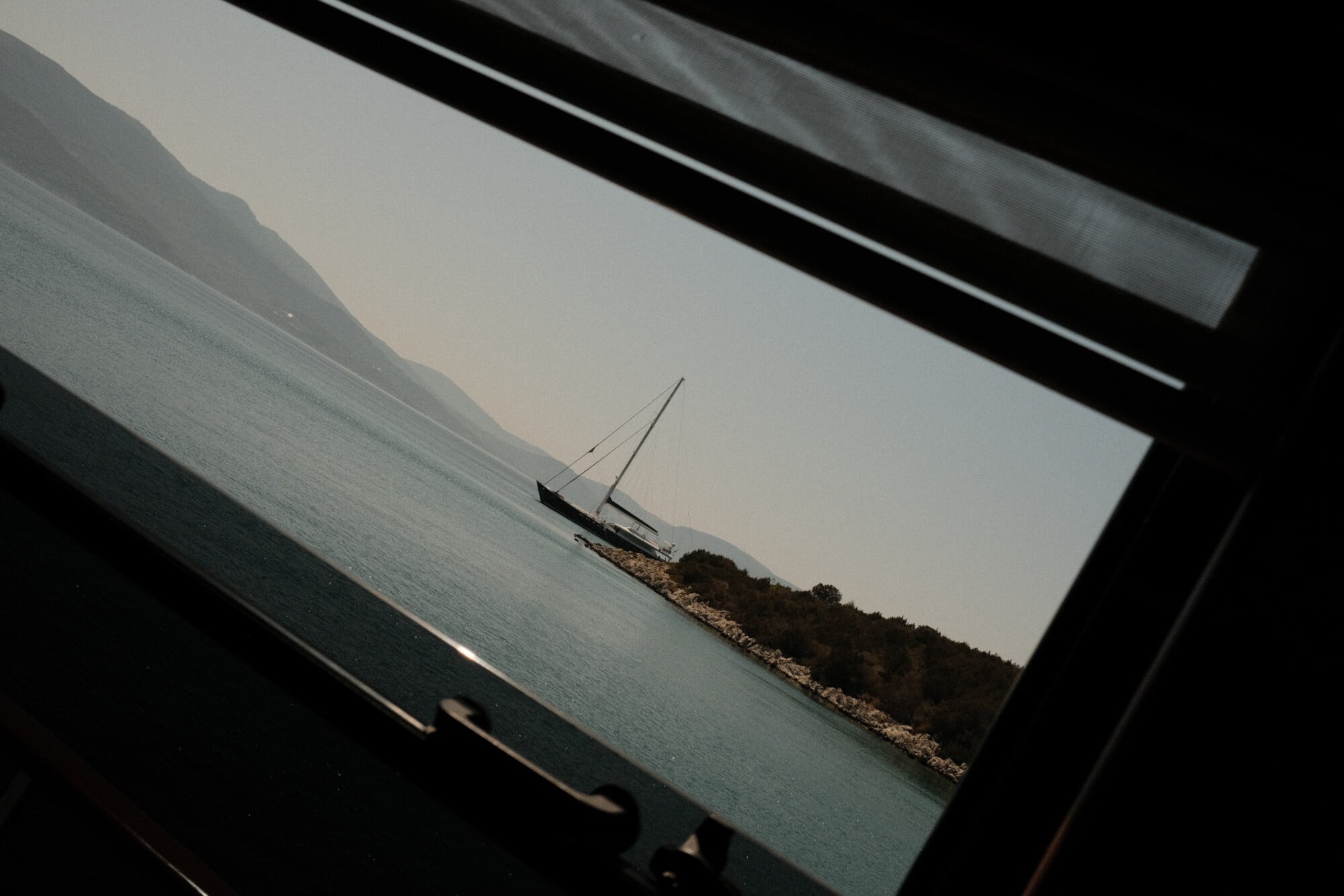 Sailing to Dalyan and Caunos — Framed photograph of moored sailing boat near rocky coastline at calm water, minimalist coastal landscape with natural light.