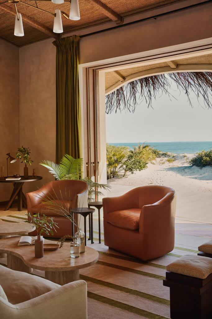 Kisawa Sanctuary, Africa — Terracotta leather armchair overlooking pristine beach, woven ceiling, olive curtains, wooden tables, coastal modernist interior design.