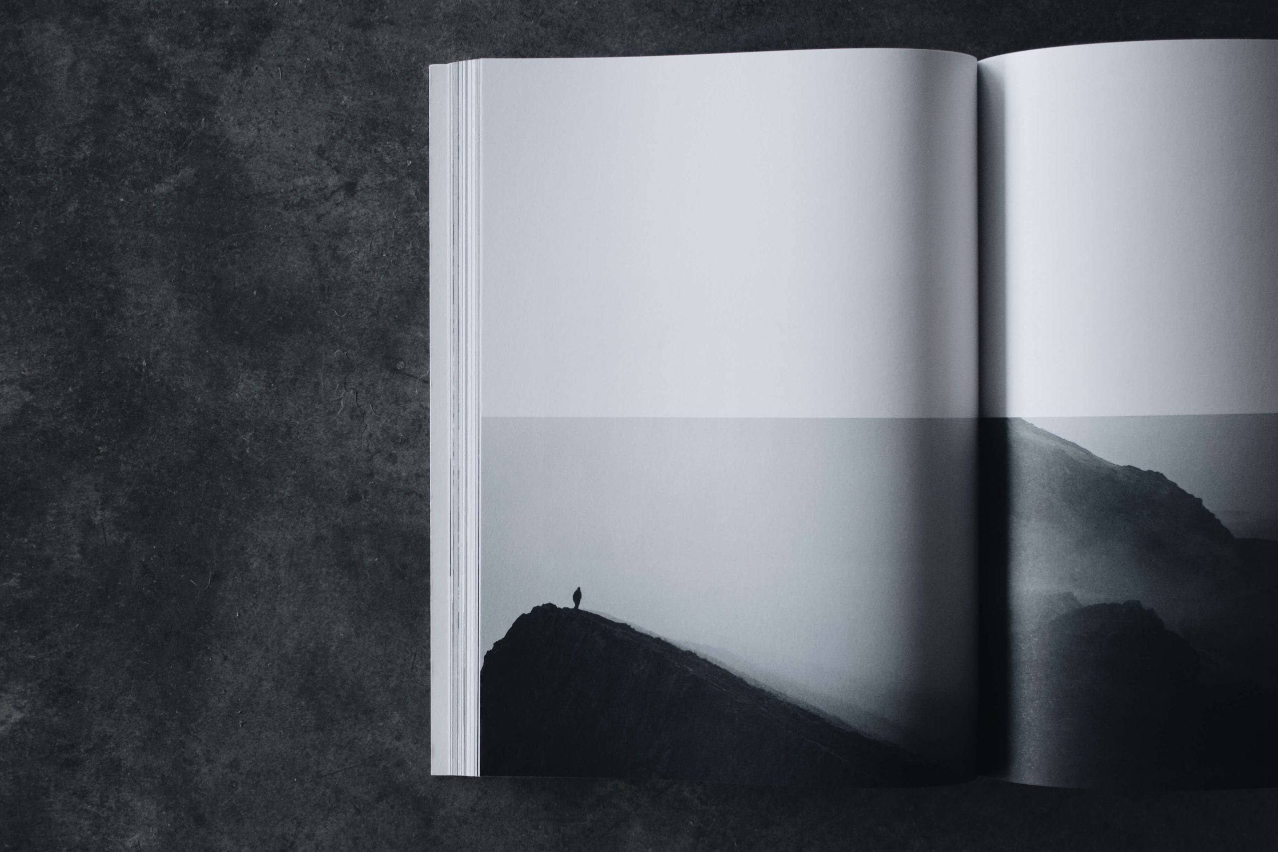 Three must-have books for design lovers — Minimalist black and white photograph of an open magazine spread featuring a solitary figure on a misty mountain landscape, embodying contemplative luxury design aesthetics.