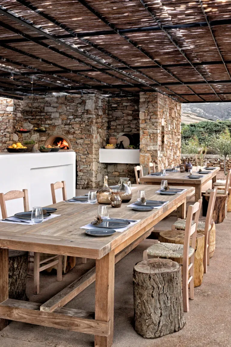 The Rooster, Europe — Covered dining terrace with long wooden table, stone walls, woven reed ceiling, and wood-fired pizza oven overlooking olive groves.