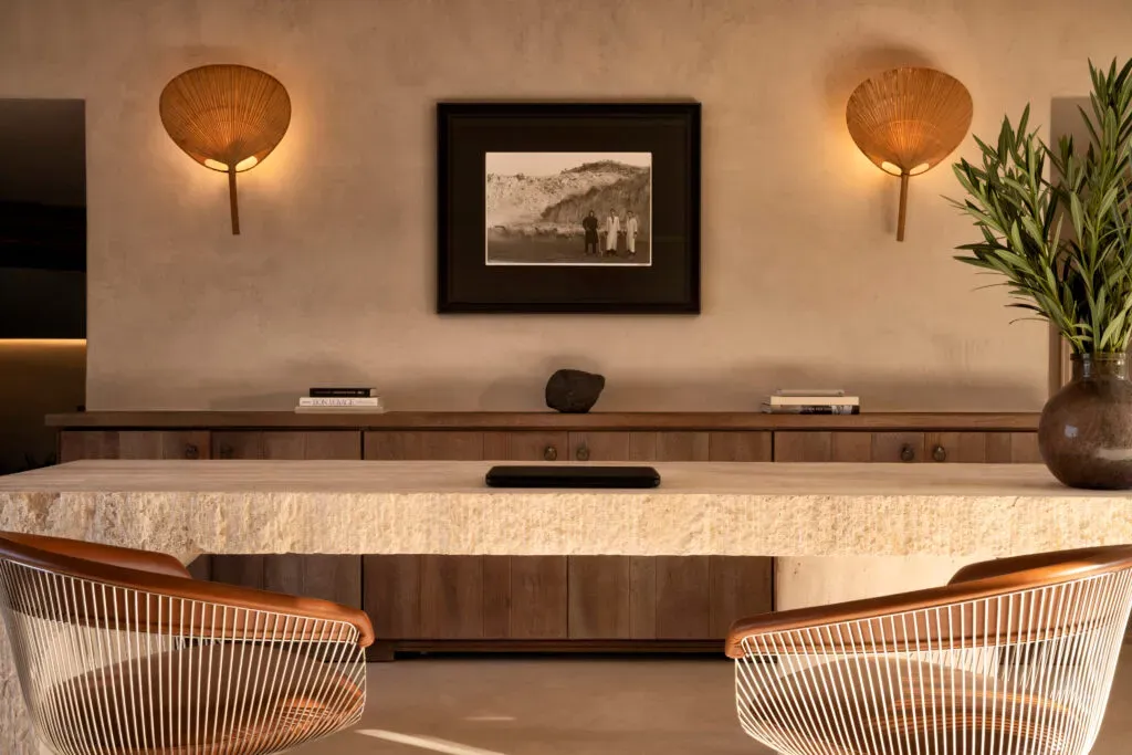 The Rooster, Europe — Curved marble reception desk with walnut cabinetry, brass shell sconces, vintage photograph, and woven chairs in minimalist luxury hospitality interior.