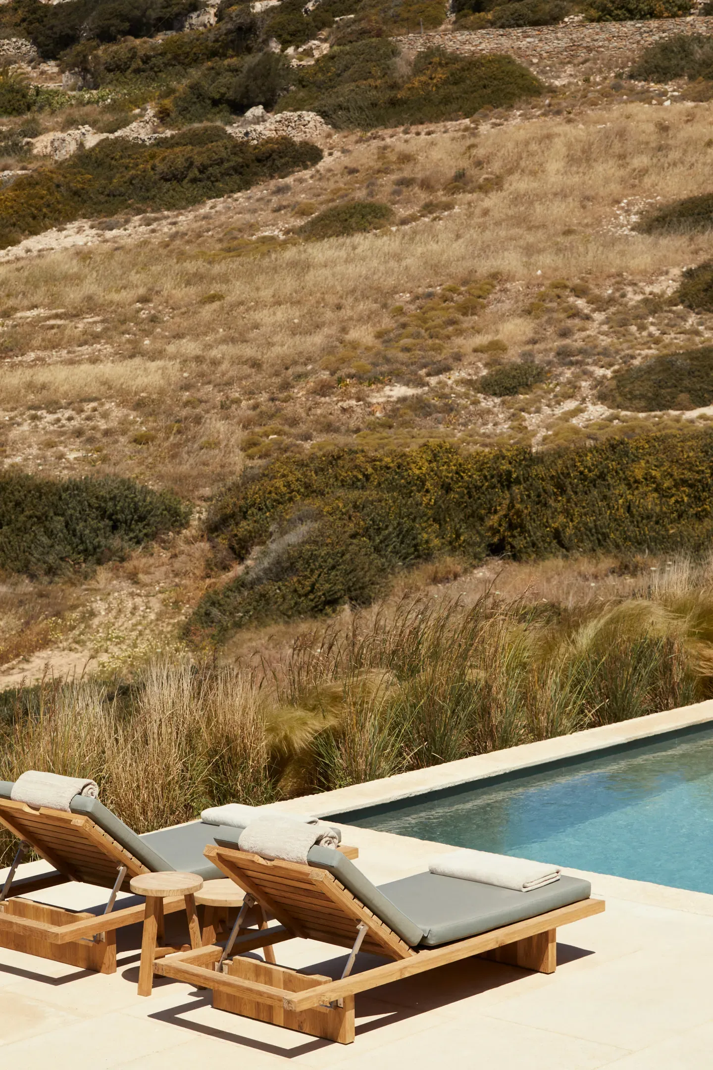 The Rooster, Europe — Teak loungers with gray cushions and side table overlook terraced hillside with native grasses and limestone outcroppings.