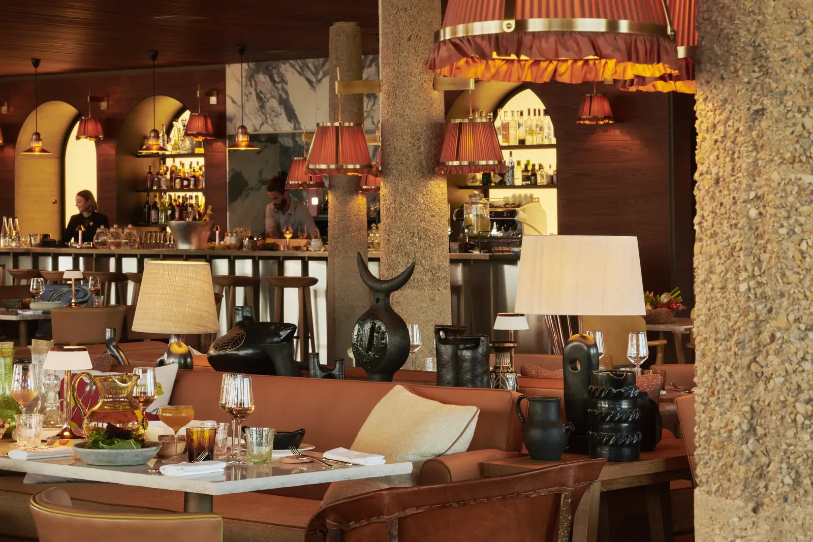 Lily of the Valley, Europe — Warm terracotta banquette seating with cream marble table, pendant red lamps, stone columns, and bar counter in contemporary luxury dining room.