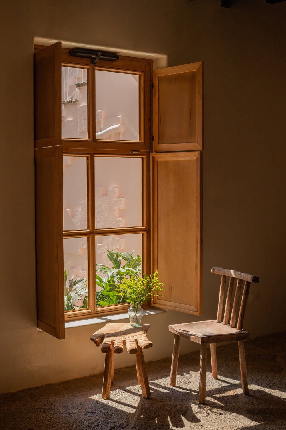 La Valise San Miguel, Mexico — Wooden shuttered window with potted plants casting shadows on terracotta walls, rustic chairs in warm natural light.
