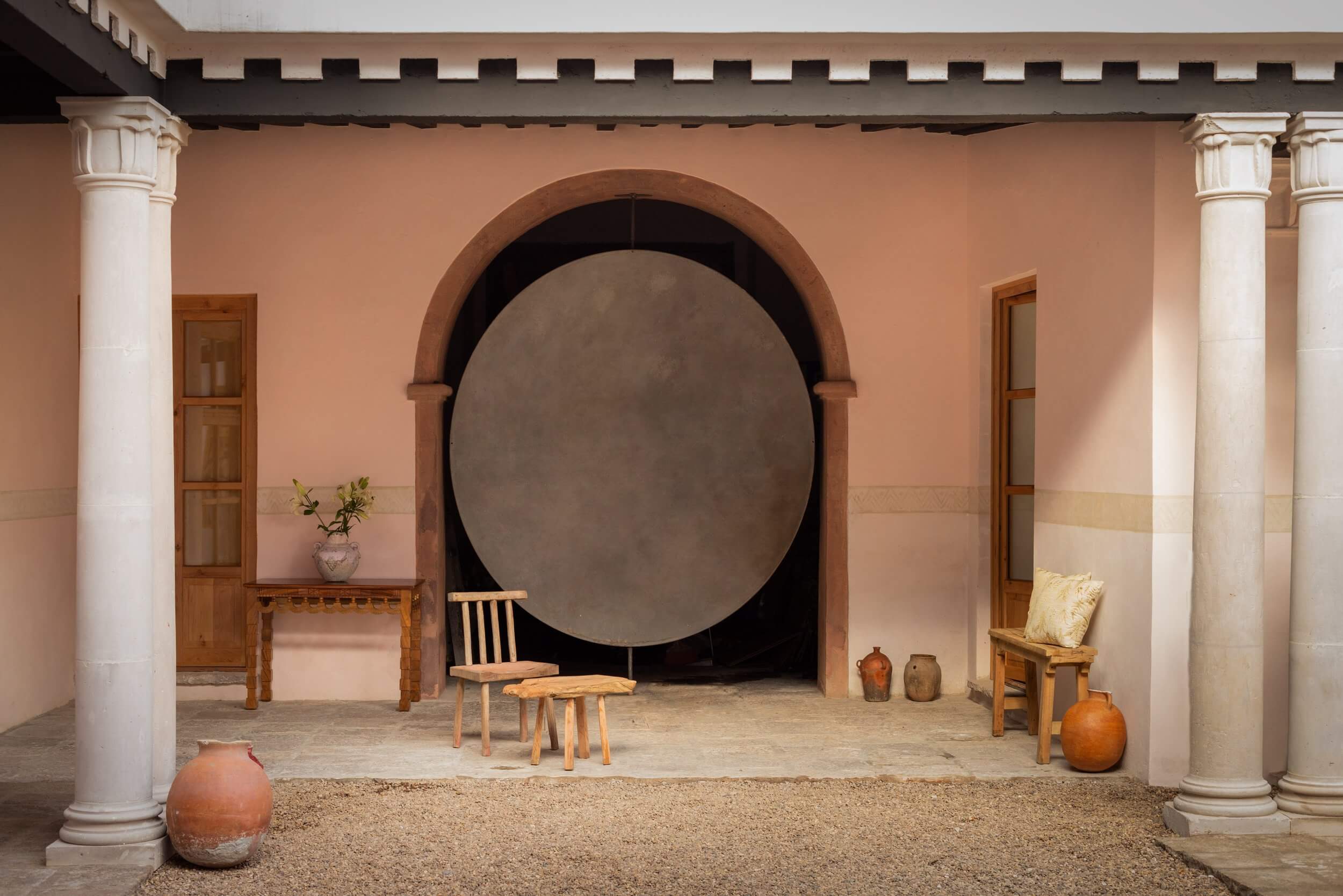 La Valise San Miguel, Mexico — Terracotta courtyard with white columns, arched doorway, wooden furniture, and ceramic vessels in warm Mediterranean light.