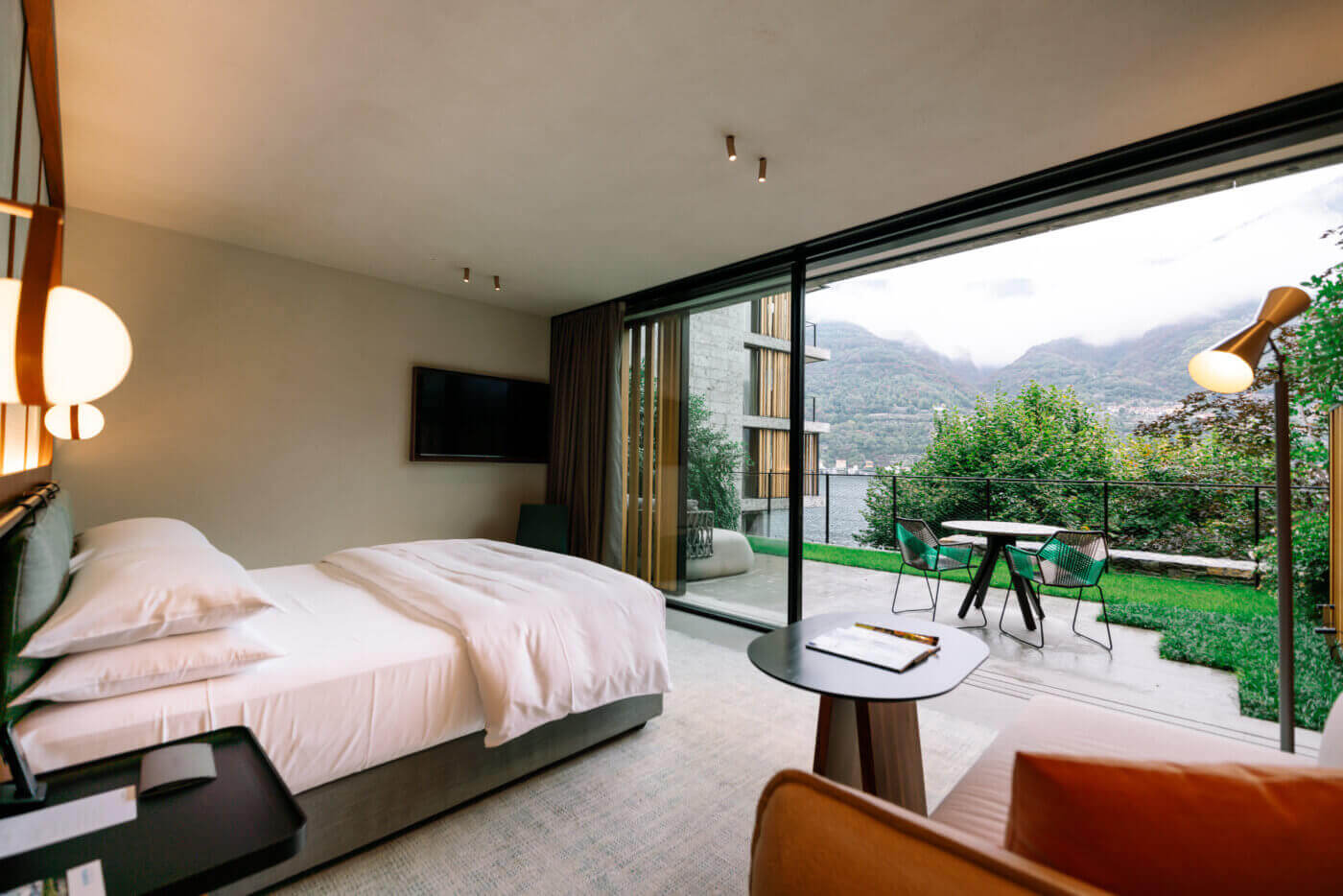 Il Sereno Lago di Como, Torno, Italy — Modern minimalist bedroom with lakeside terrace, mountain views, sculptural lighting, and contemporary furnishings overlooking Alpine landscape.