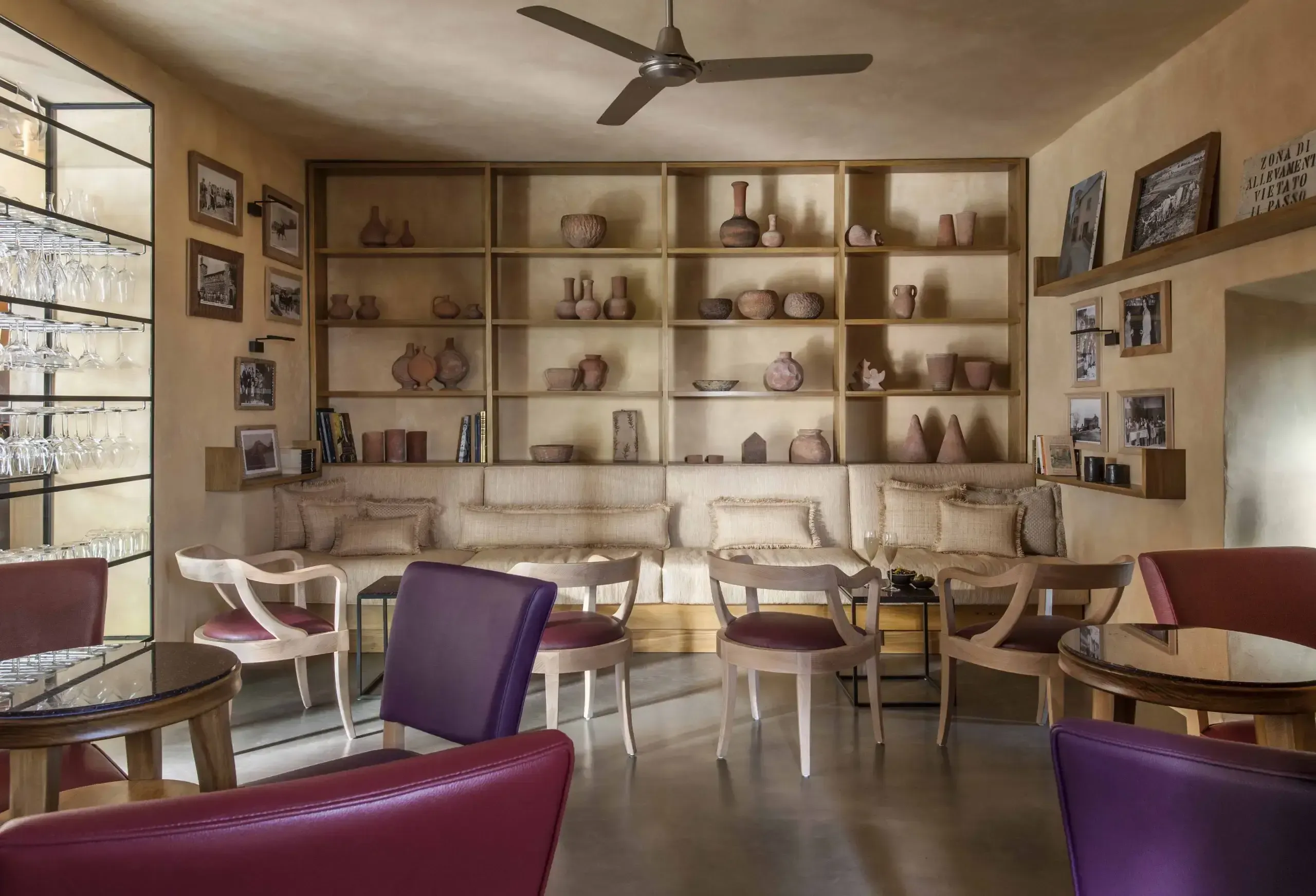 Library Bar, Europe — Warm-toned lounge with terracotta pottery displays, burgundy leather chairs, natural light, and curated shelving in luxury hospitality setting.