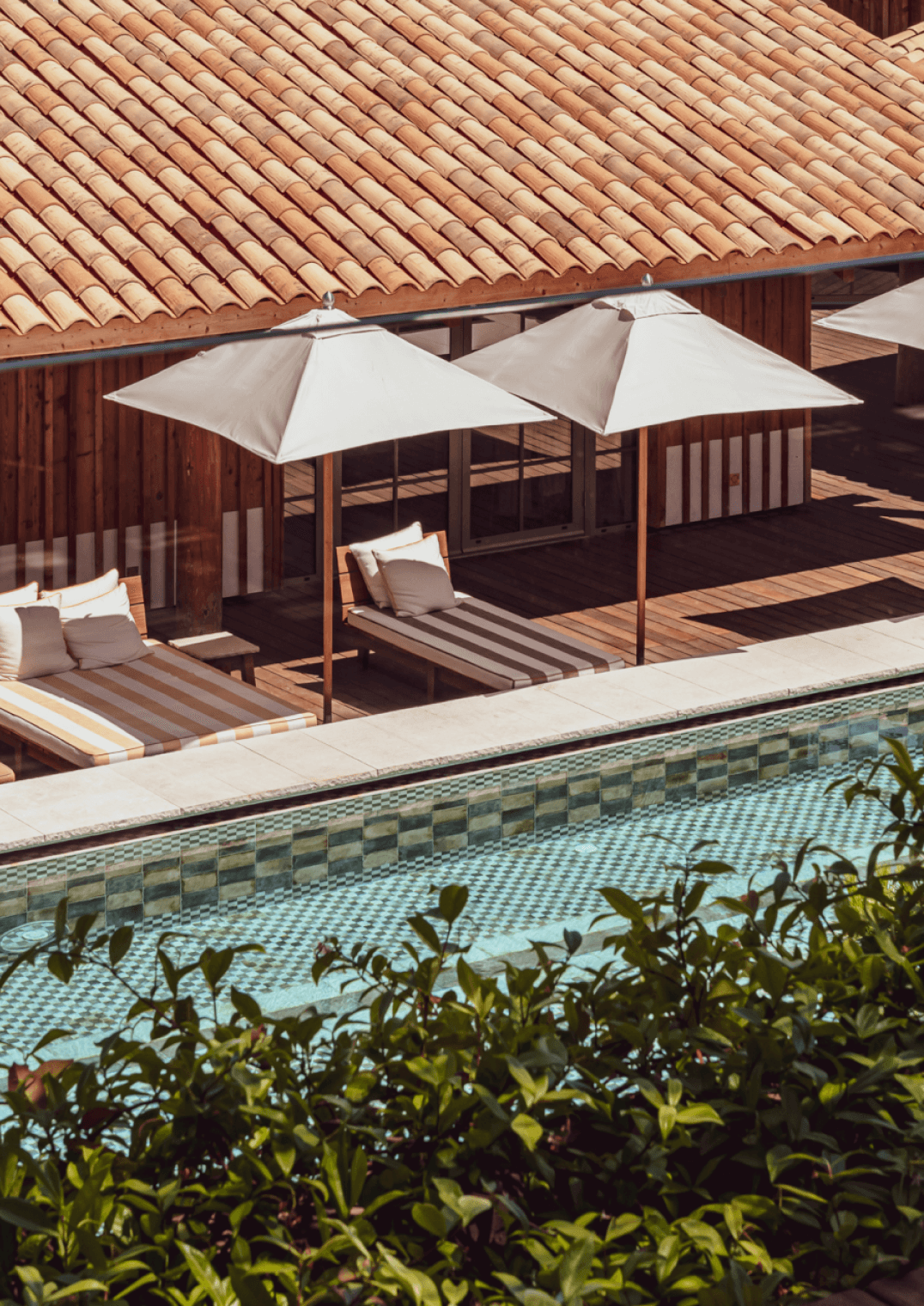 Lily of the Valley, Europe — Poolside terrace with clay tile roof, striped loungers beneath cream umbrellas, geometric tile pool edge, warm afternoon light.